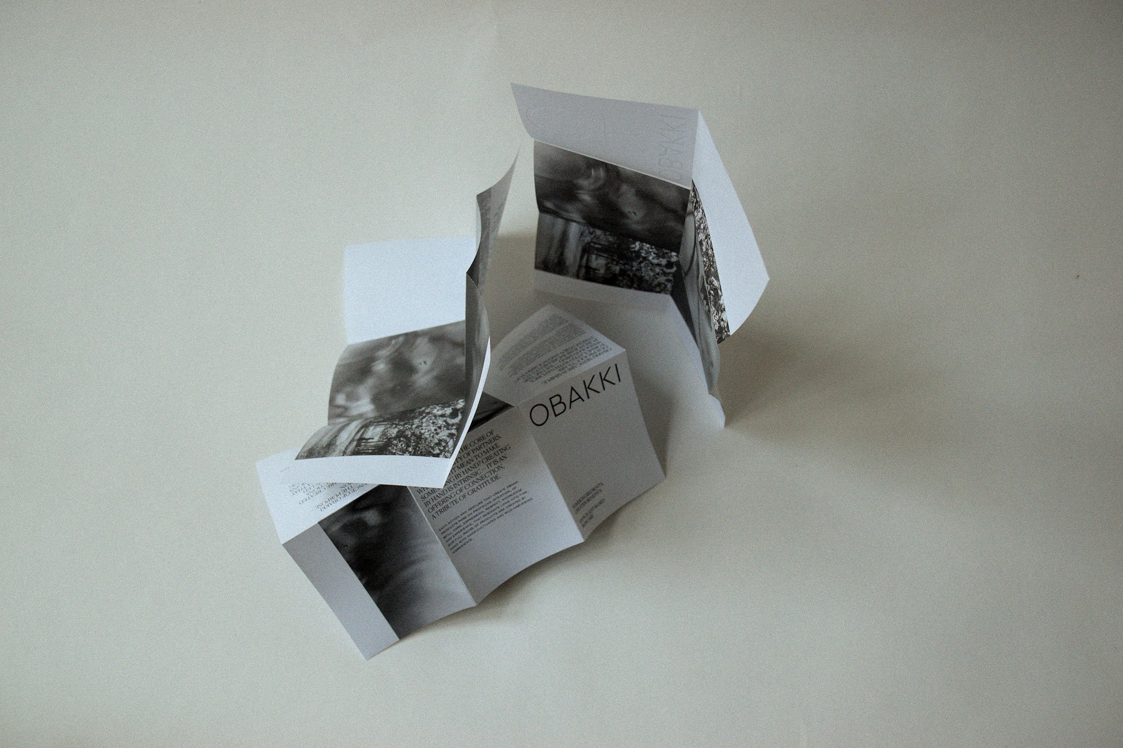 An unfolded scored brochure or paper with black and white nature images and text, including the name 'OBAKKI'.