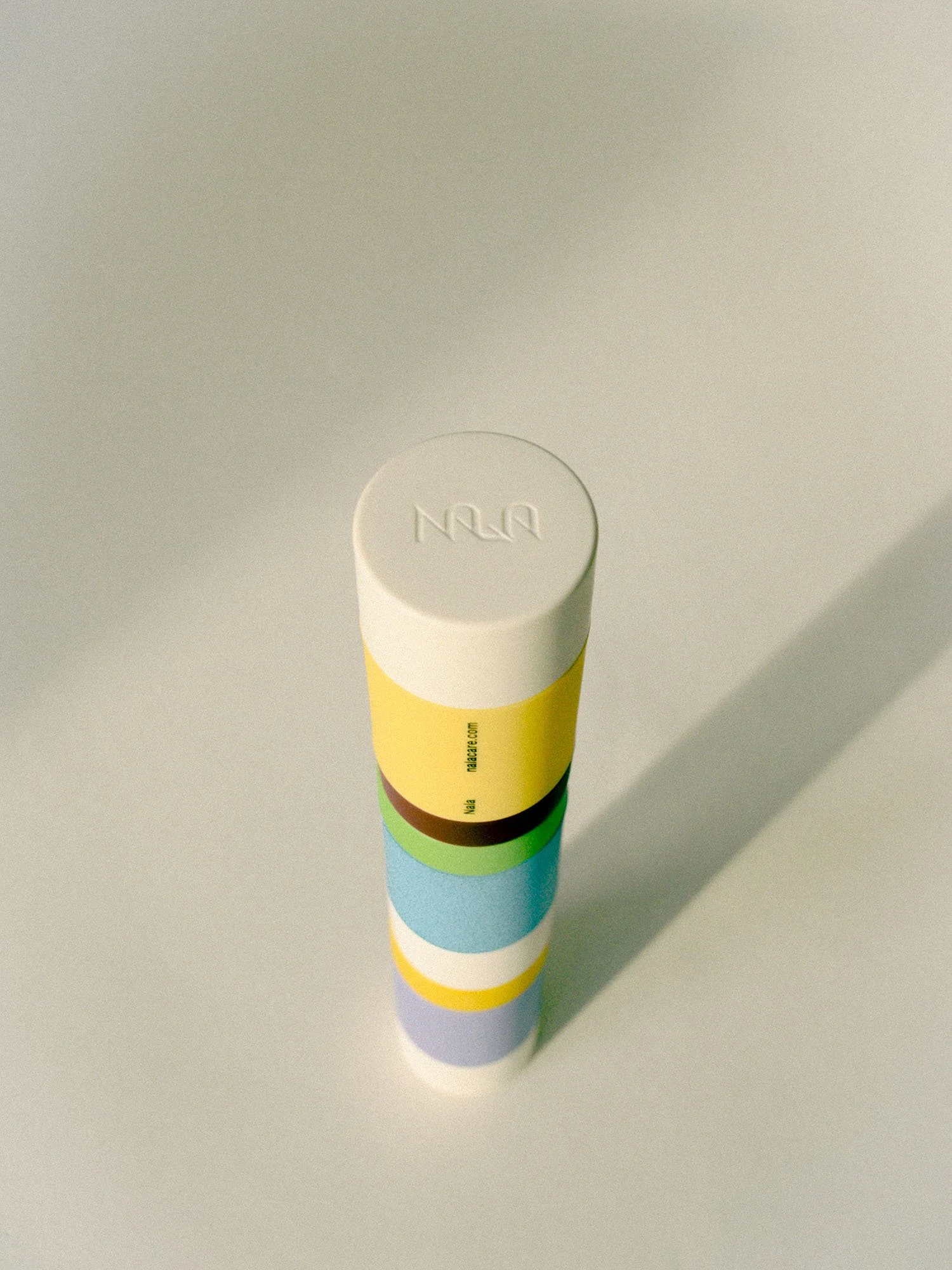 Stack of colorful cylindrical tablets on a light surface, casting a shadow.