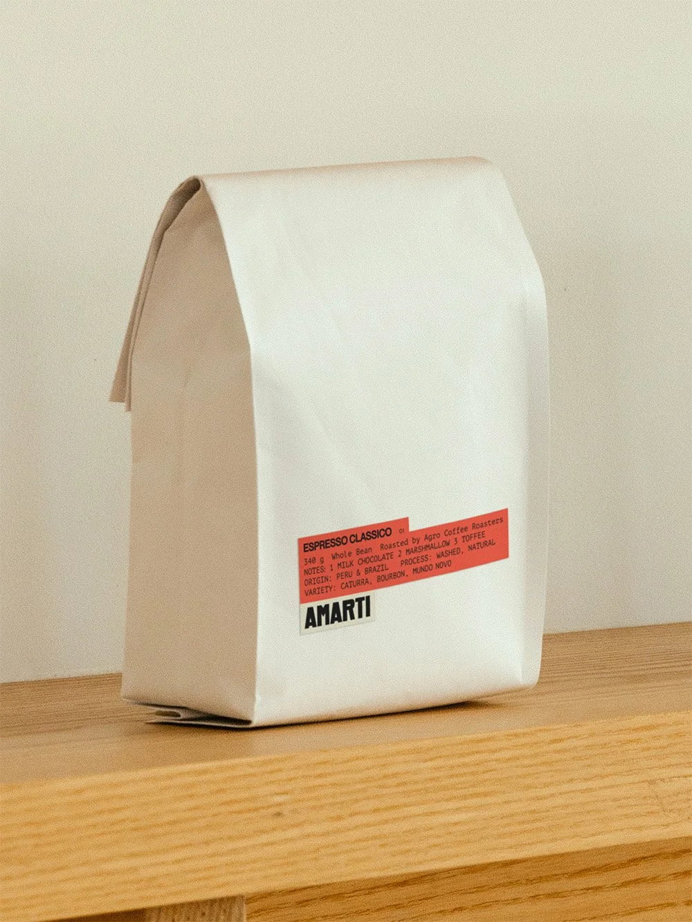 A white paper bag of Amarti coffee with a red label, placed on a wooden surface against a plain background.