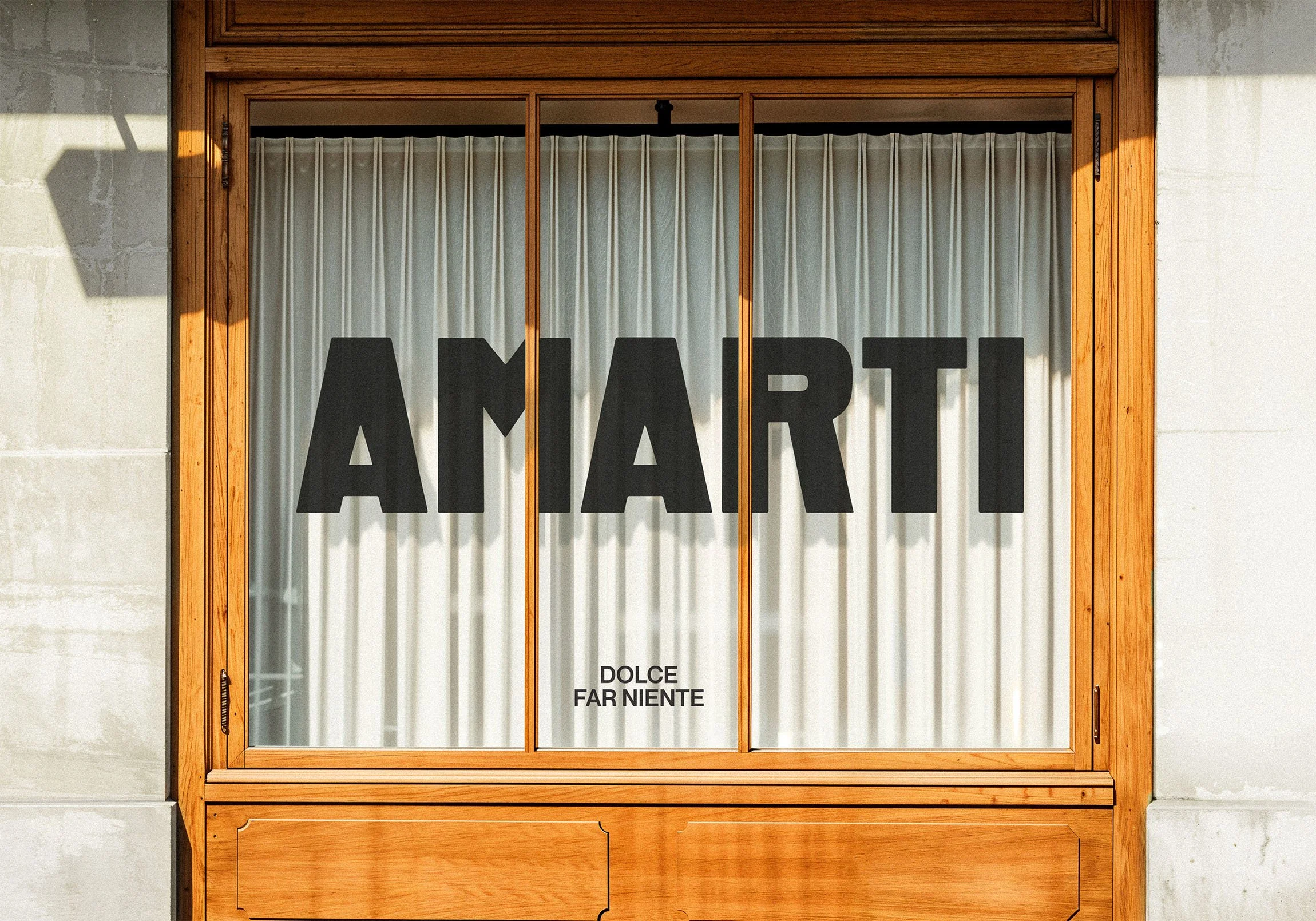 Storefront window with wooden frame, white curtains, and large black vinyl letters spelling 'AMARTI' on the glass. Small text below reads 'DOLCE FAR NIENTE'.