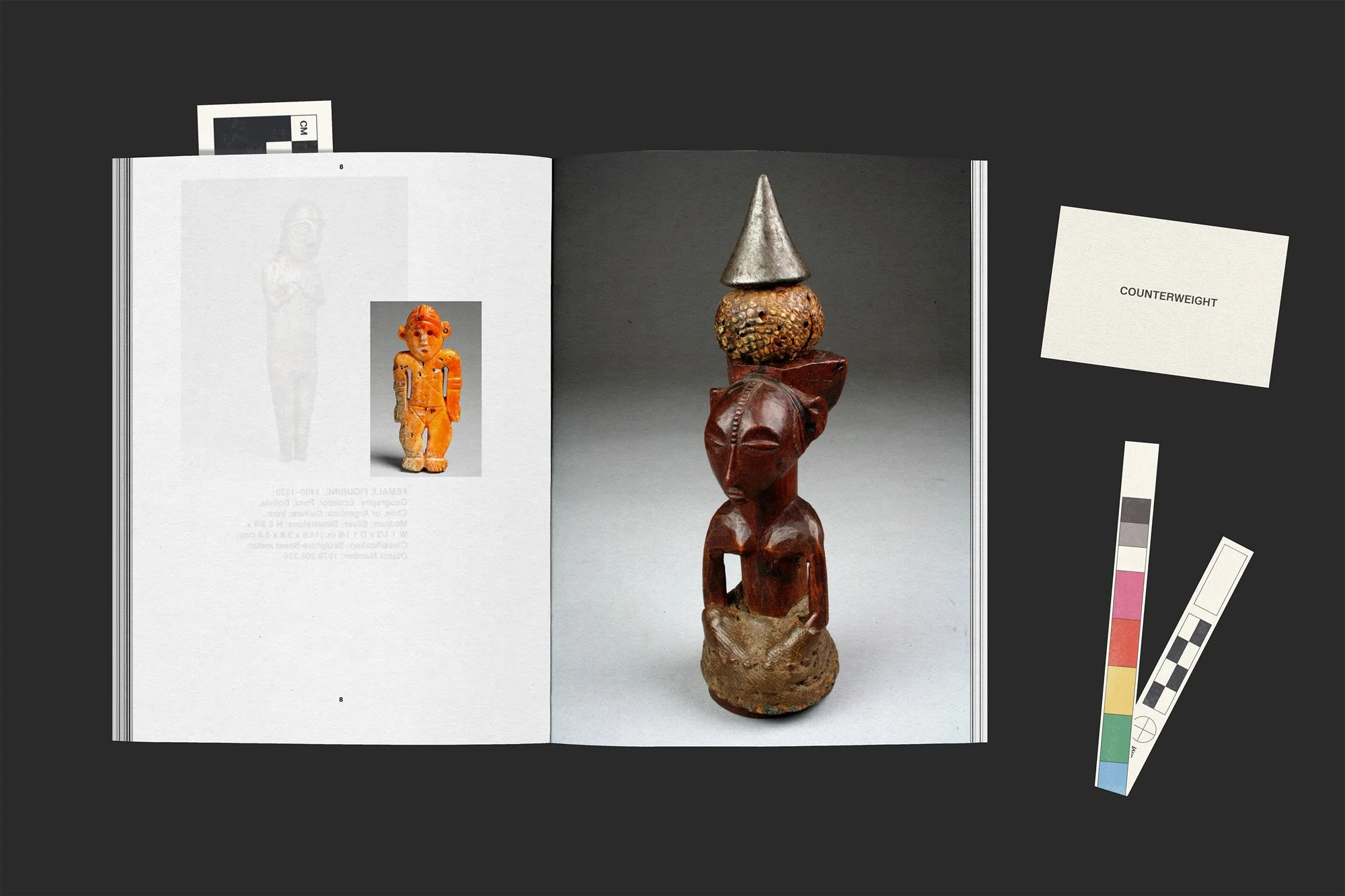 Open book displaying a photograph of a wooden sculpture of a human figure from Congo with a conical object on its head, surrounded by a color calibration tool-inspired bookmark and a card that reads "revealed" on a black background.
