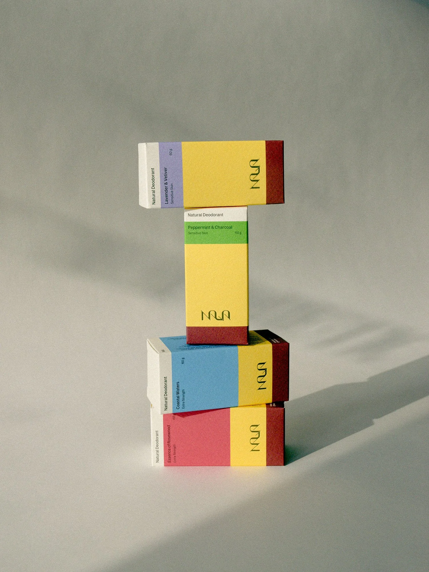 Stacked boxes of natural deodorant with different colored packaging in orange, blue, green, yellow, and white, casting a shadow on a plain surface.
