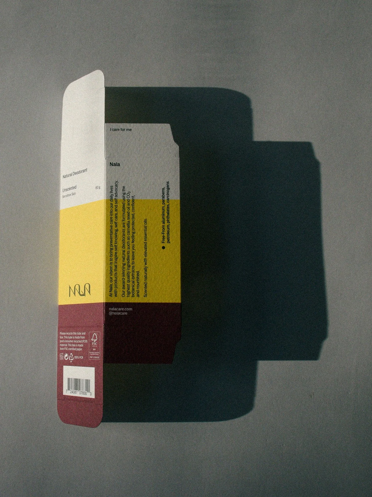 An empty and open box of Nala natural deodorant box on a gray surface, casting a shadow.