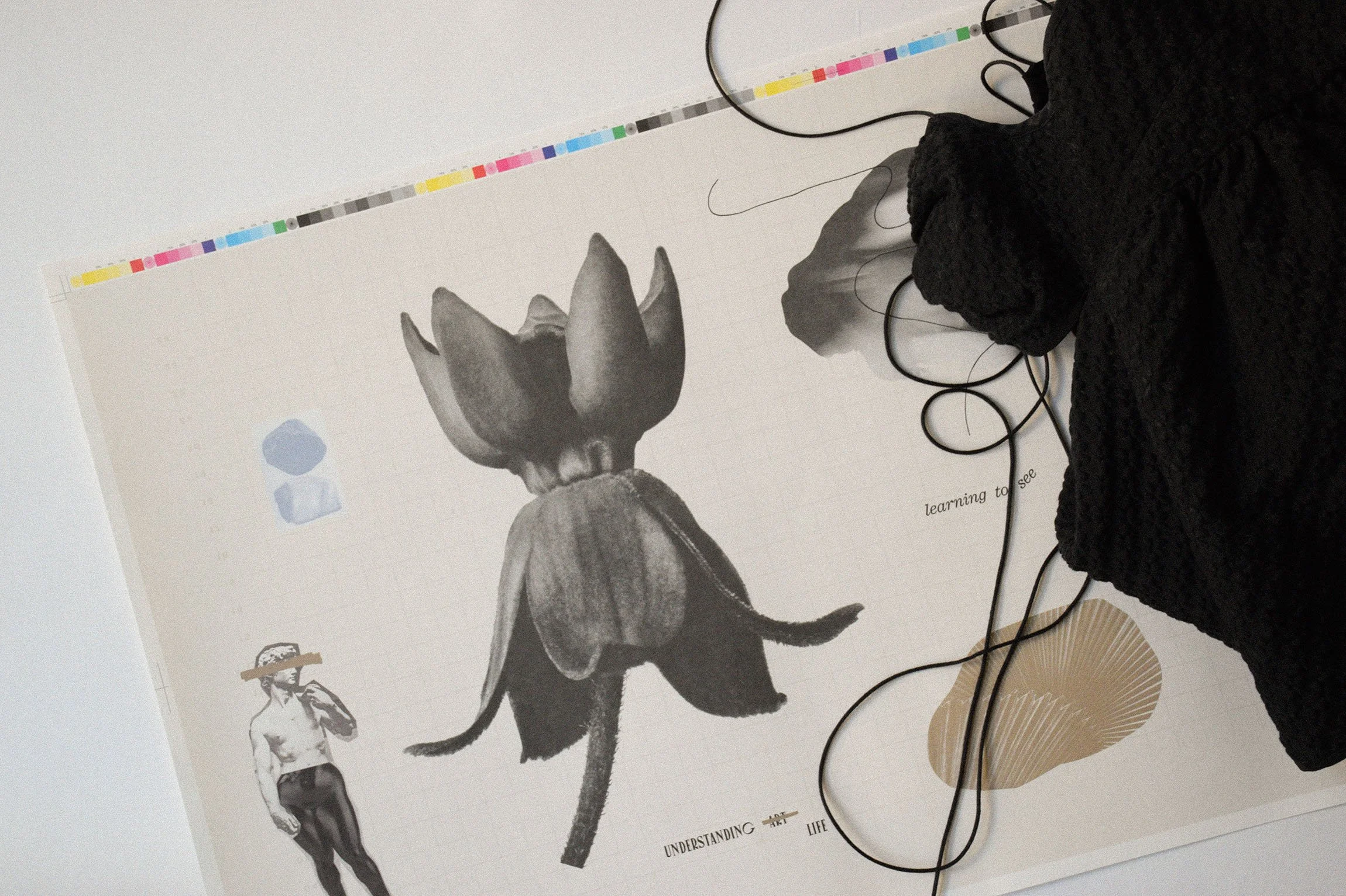 A paper wrap with collage artwork showing a large flower with petals resembling a tulip, a statue figure, and abstract shapes with floral photos inside. A black top with many thin strings lays in a pile on top.