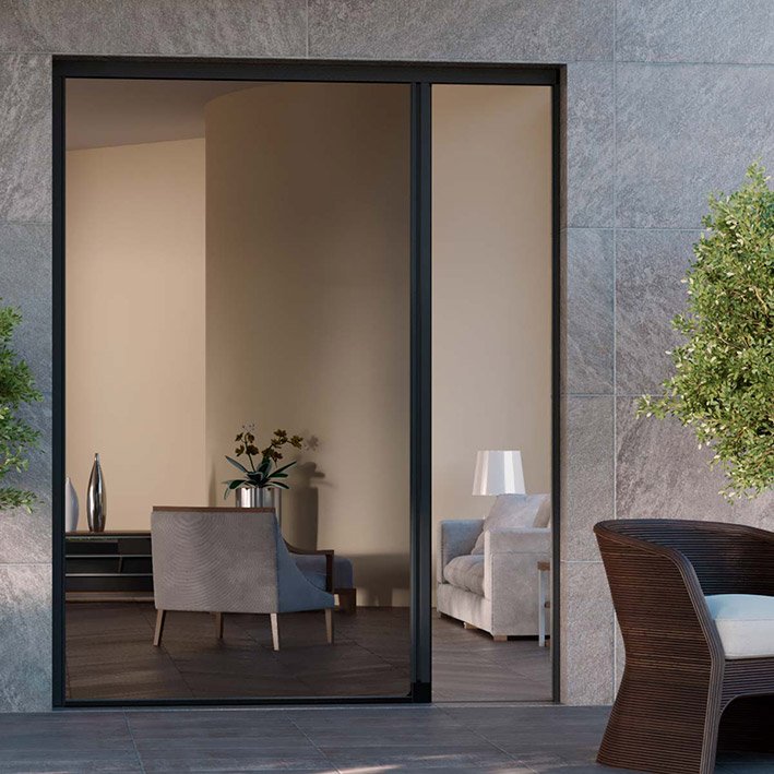 Porta finestra scorrevole con vista su salotto moderno con divano, poltrona e lampada. Pianta decorativa all'esterno.