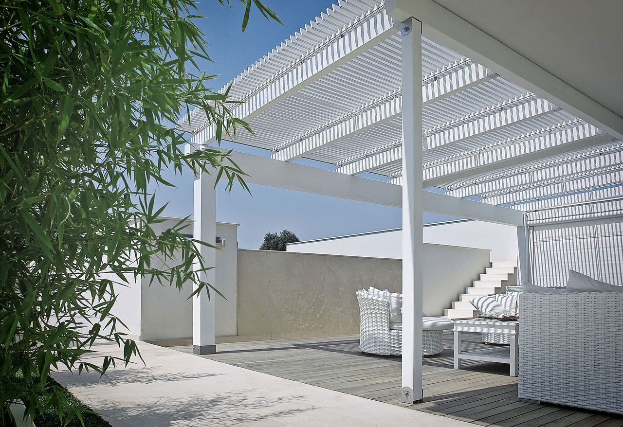 Terrazza moderna con pergola bianca, arredi intrecciati e vegetazione di bambù.