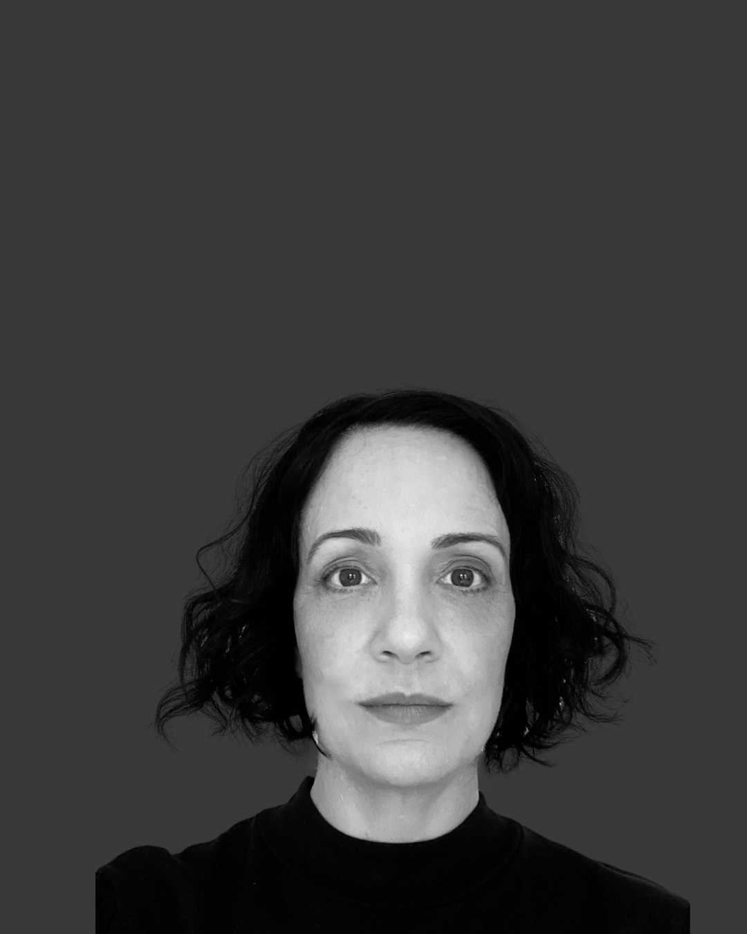 Black and white portrait of a person with short, dark hair and a neutral expression, wearing a dark top, set against a plain background.