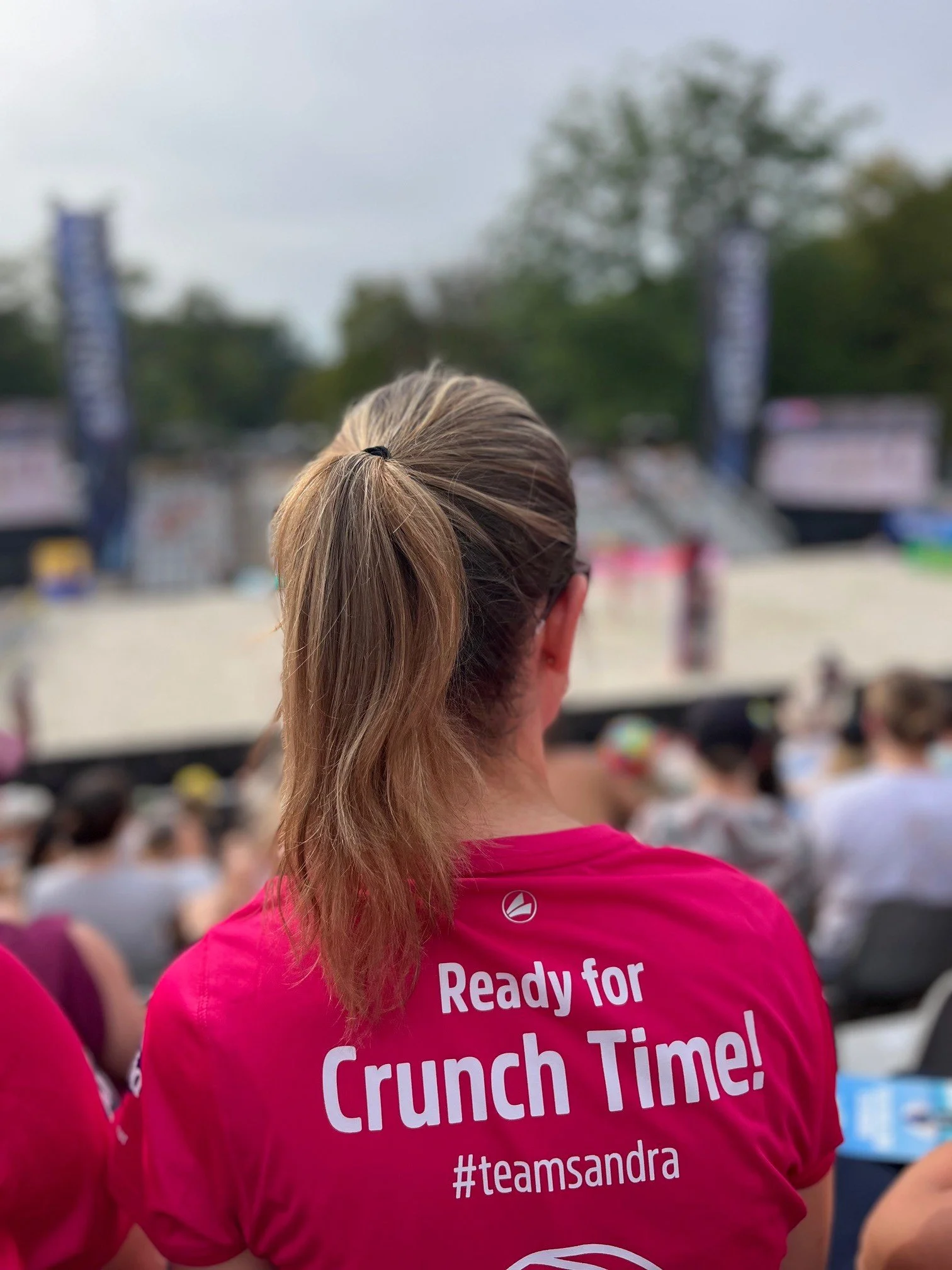 Beachvolleyball-Spielerin im pinken Team-Sandra-Shirt mit Alpia Crunch Time Aufdruck bei einem Beachvolleyball-Turnier.