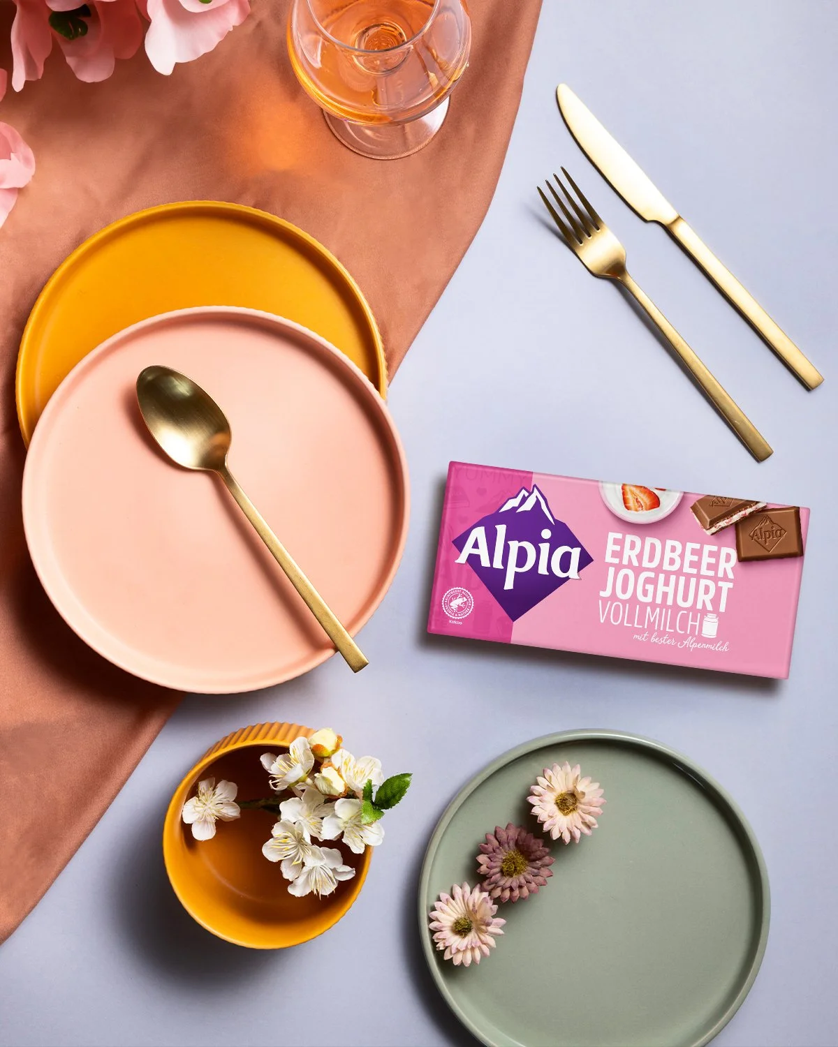 Alpia Erdbeer-Joghurt Tafel auf dekoriertem Tisch – Fruchtig-cremiger Schokoladengenuss im stilvollen Interior-Setting mit Blume und Geschirr.