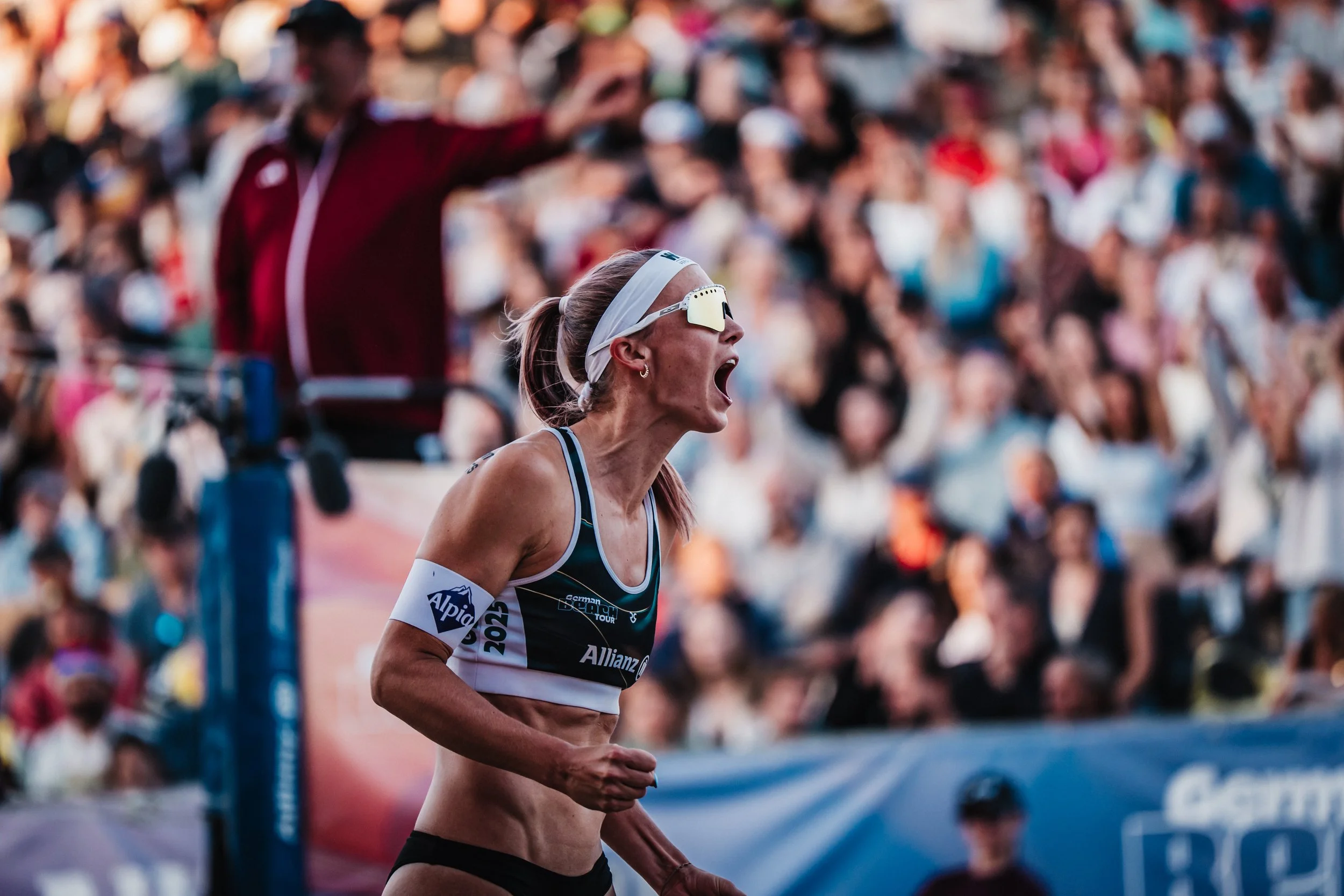 Beachvolleyball-Nationalspielerin Sandra Ittlinger jubelt bei einem Turnier vor Publikum und trägt ein Trikot mit Alpia Sponsorenlogo.