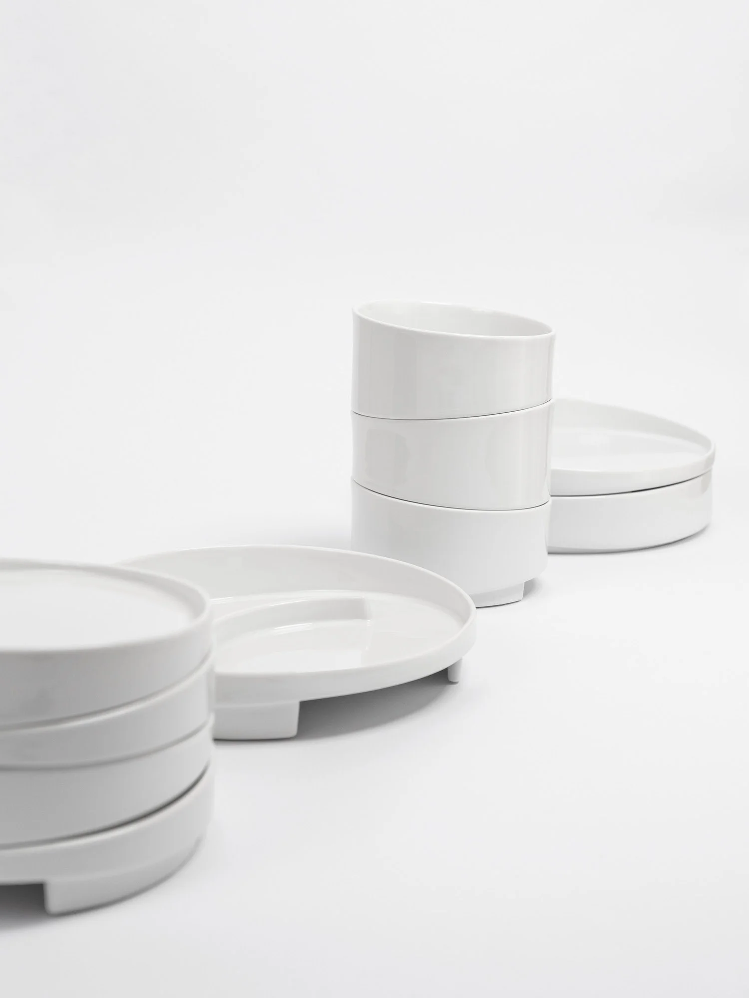 Weiße porzellan Teller und Schalen sind von Links nach rechts ins Bild hinein platziert. Das Geschirr ist hübsch gestapelt und ergibt mit der schrägen Form ein schönes Muster.