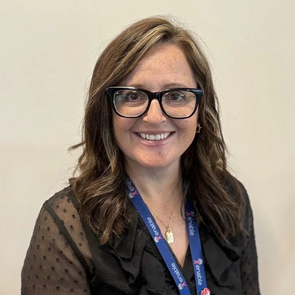 Woman smiling with glasses and black blouse smiling against a plain background