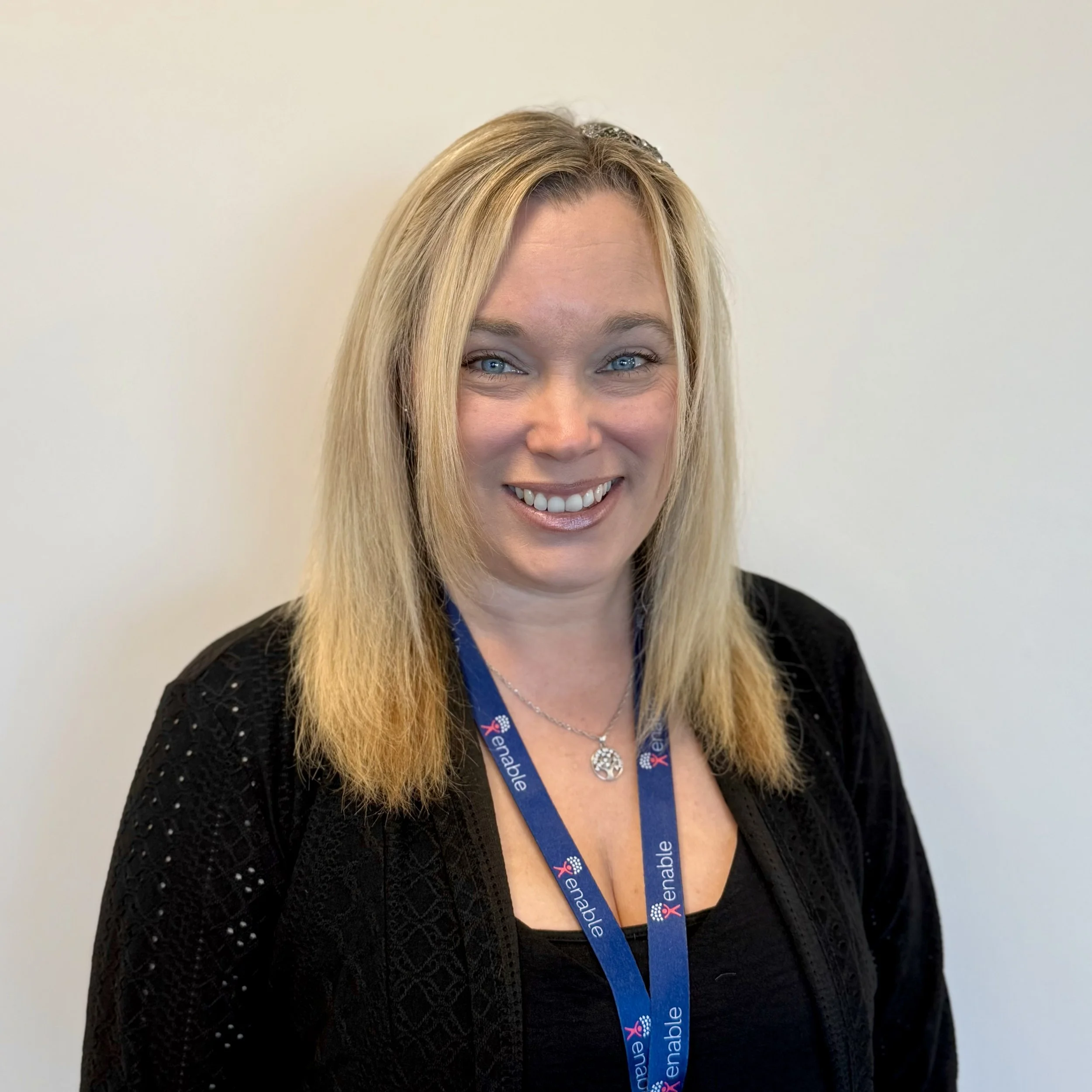 Woman with short blonde hair wearing a lanyard and black shirt against a light background.
