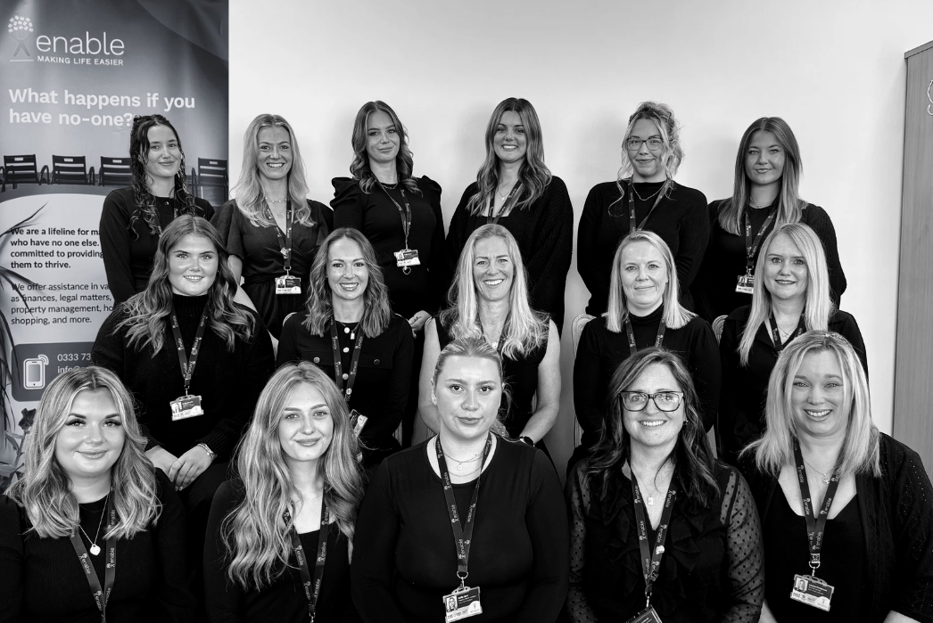 The enable team wearing similar dark attire with lanyards, posing at their chichester office in front of banners with Enable tagline -  "enable making life easier."