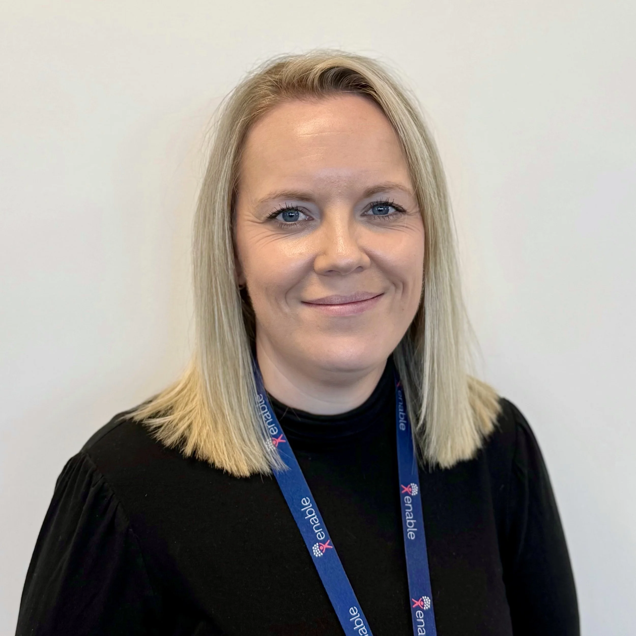 Smiling woman with short blonde hair wearing a black top and a blue 'Enable' lanyard.