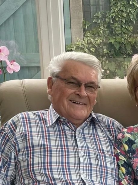 An older man with grey hair and glasses smiling wearing a checked shirt.