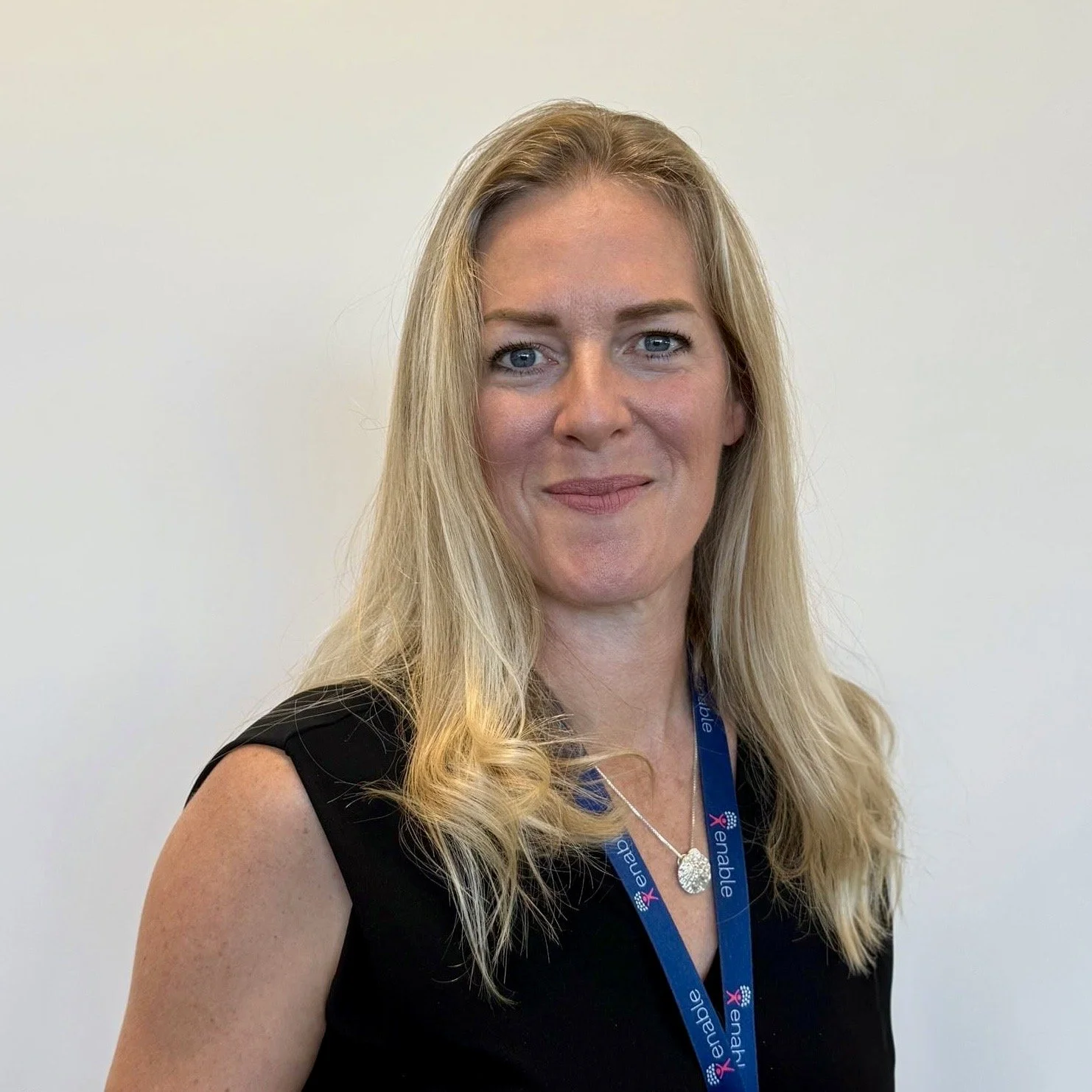 Woman with long blonde hair smiling wearing a black top and a blue lanyard with "Enable" text.