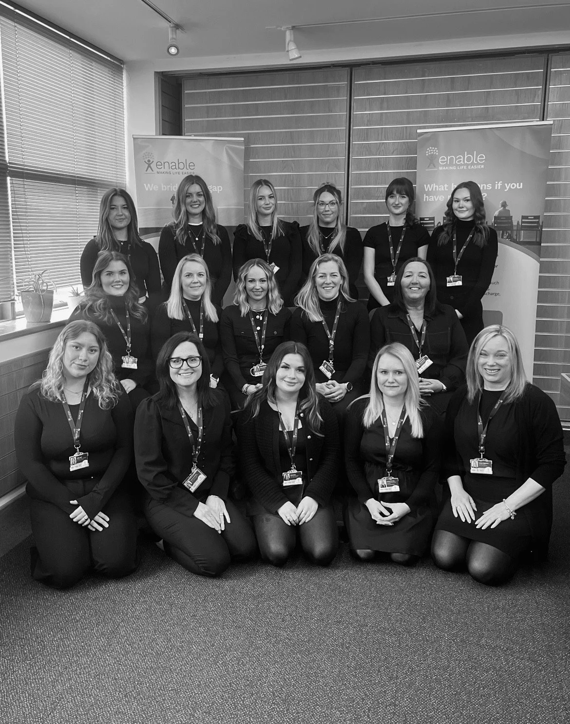 The enable team wearing similar dark attire with lanyards, posing at their chichester office in front of banners with Enable tagline -  "enable making life easier."
