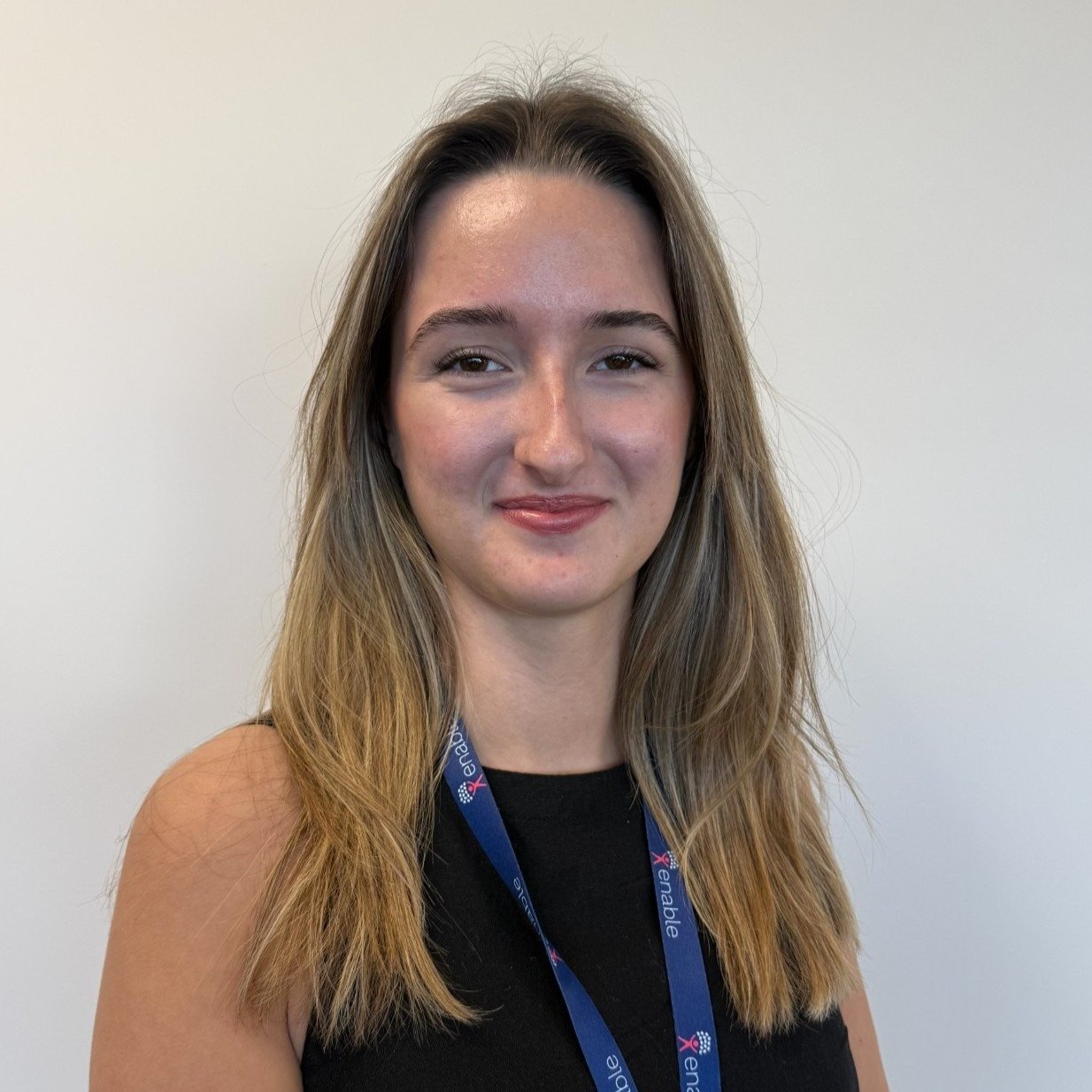 A person with long brown hair, smiling with a blue lanyard on against a plain white background.