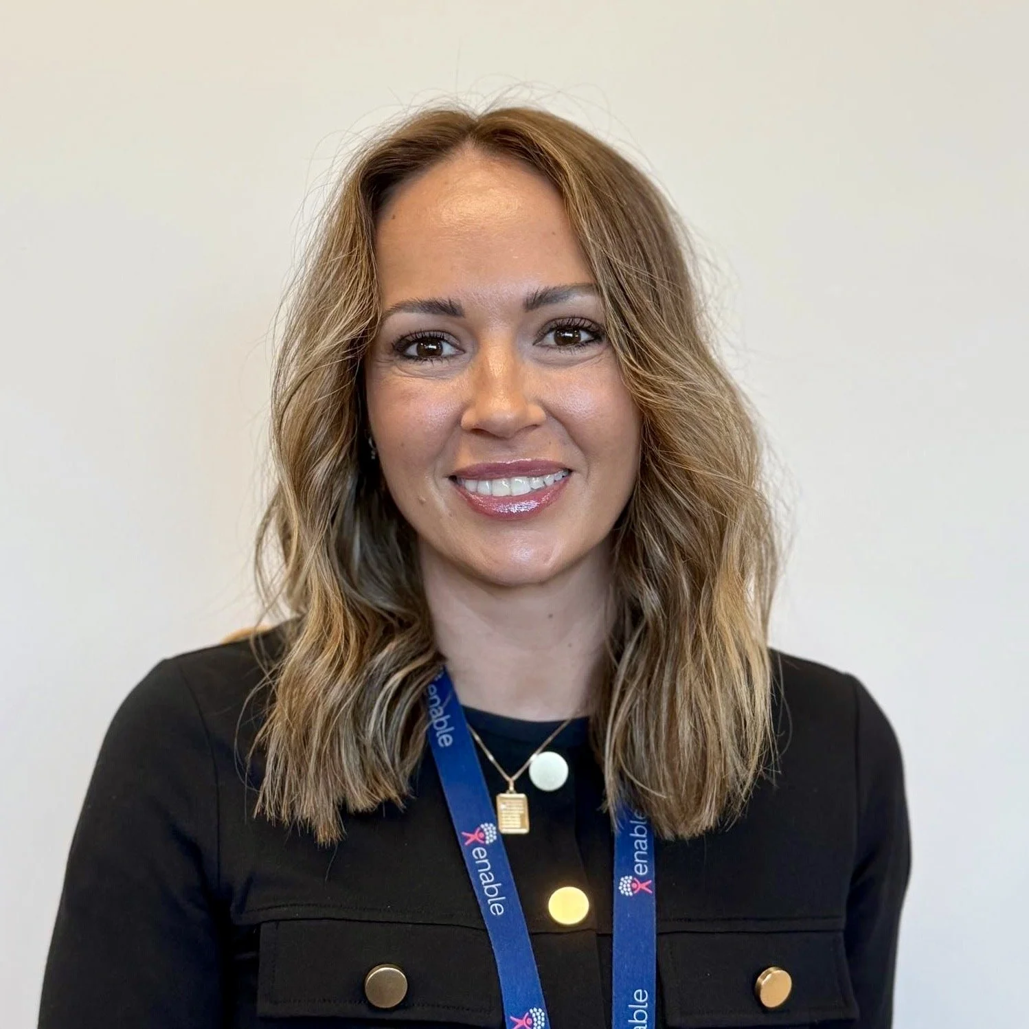 Woman smiling with short brown hair wearing a black top and blue 'Enable' lanyard.