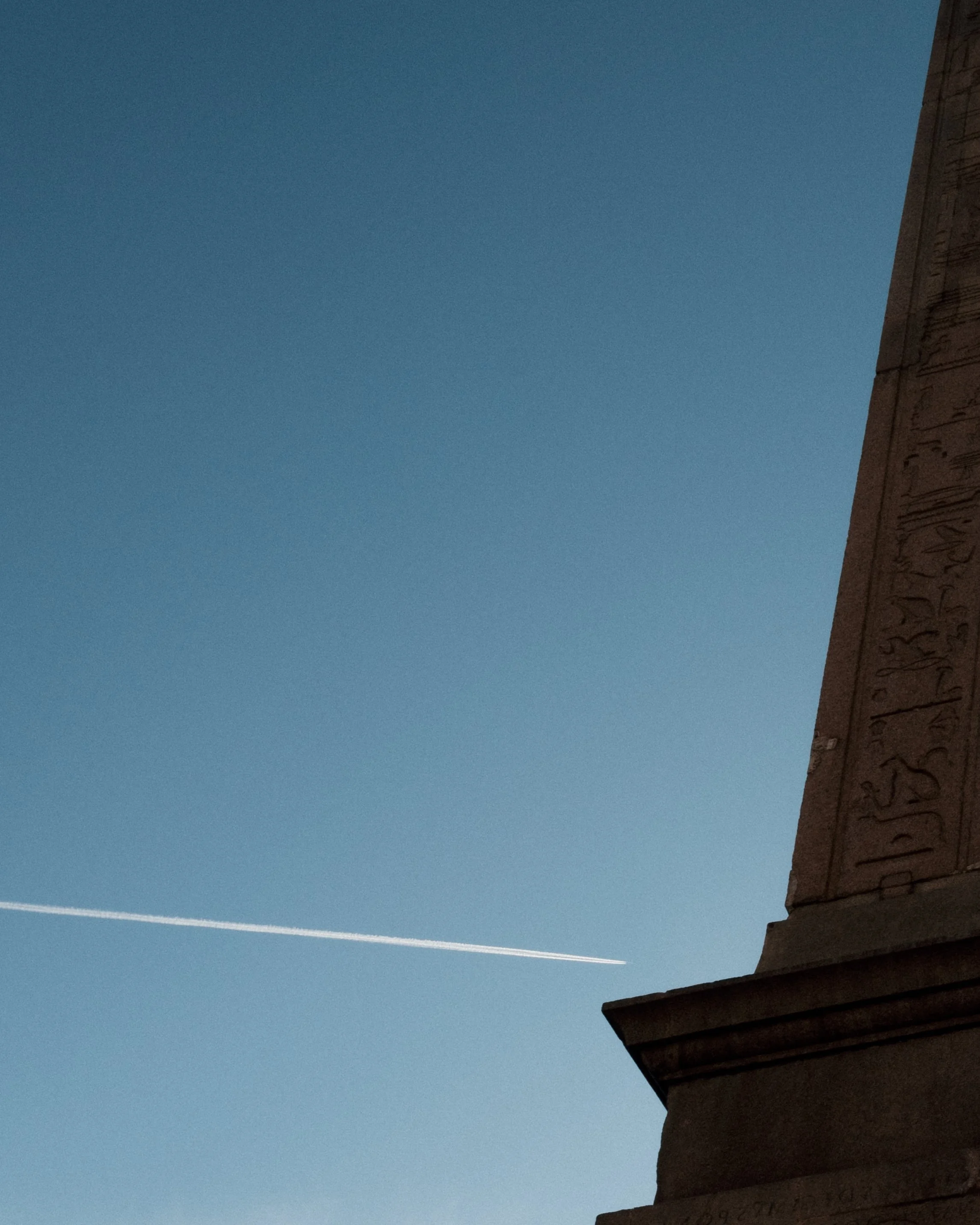 Night sky with a contrail streaking across, visible from the corner of a building with hieroglyphic carvings.