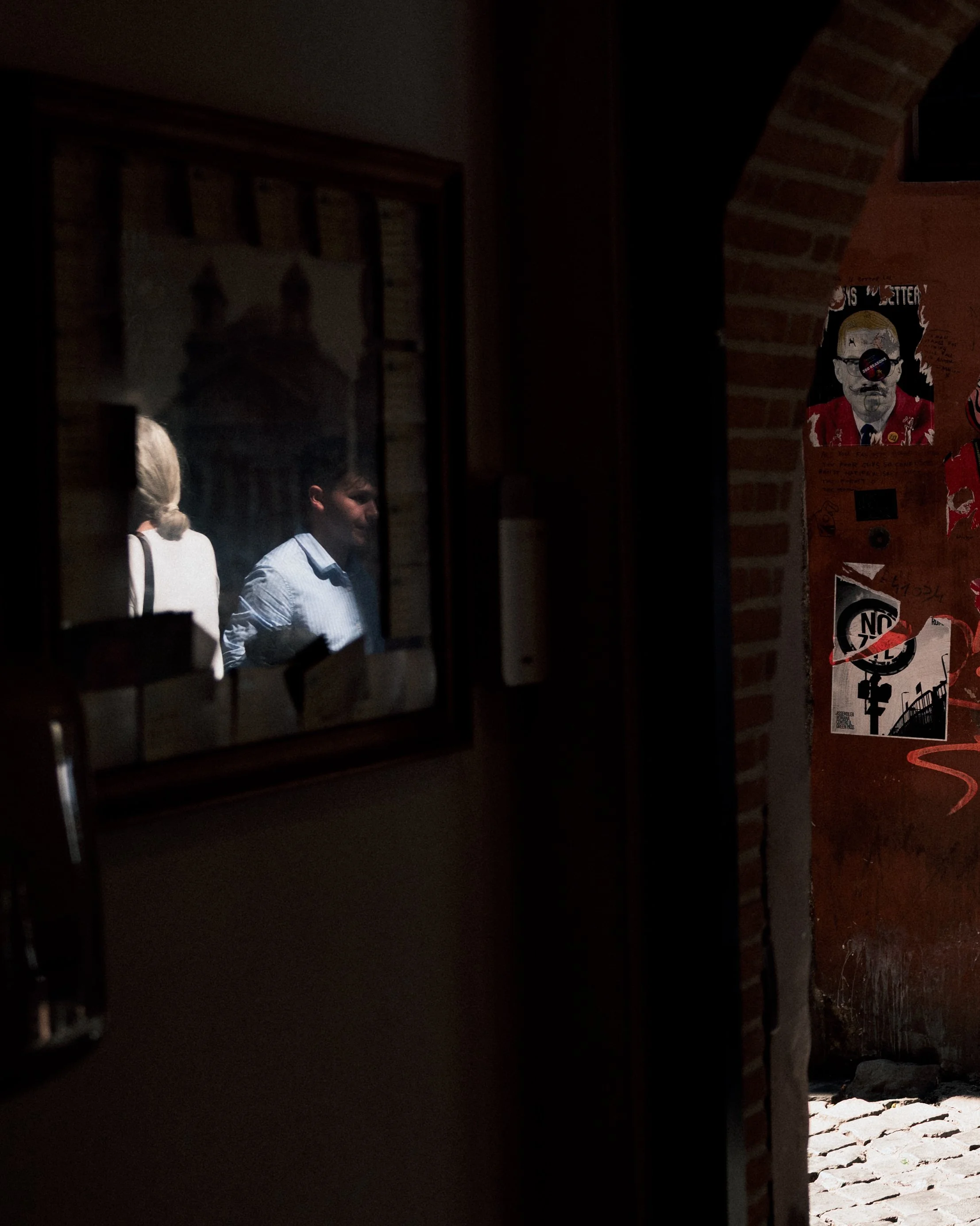 A dimly lit view through an arched brick opening showing cobblestone ground outside and a poster on the brick wall inside.