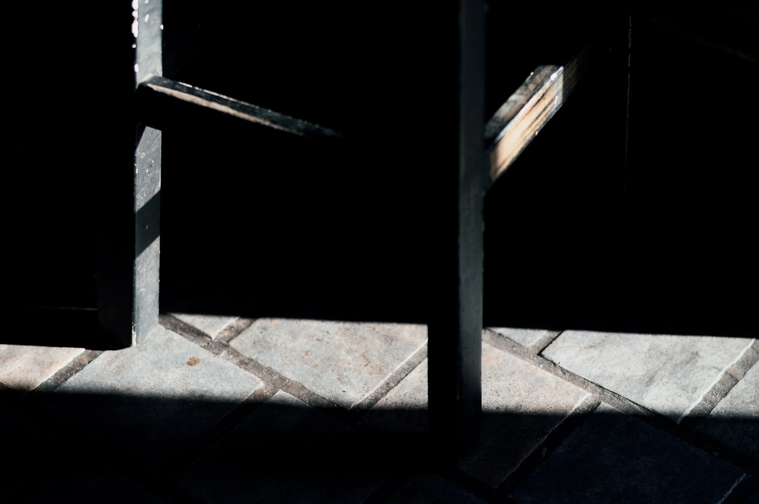 Part of a black metal chair with sunlight casting shadows on a tiled floor.