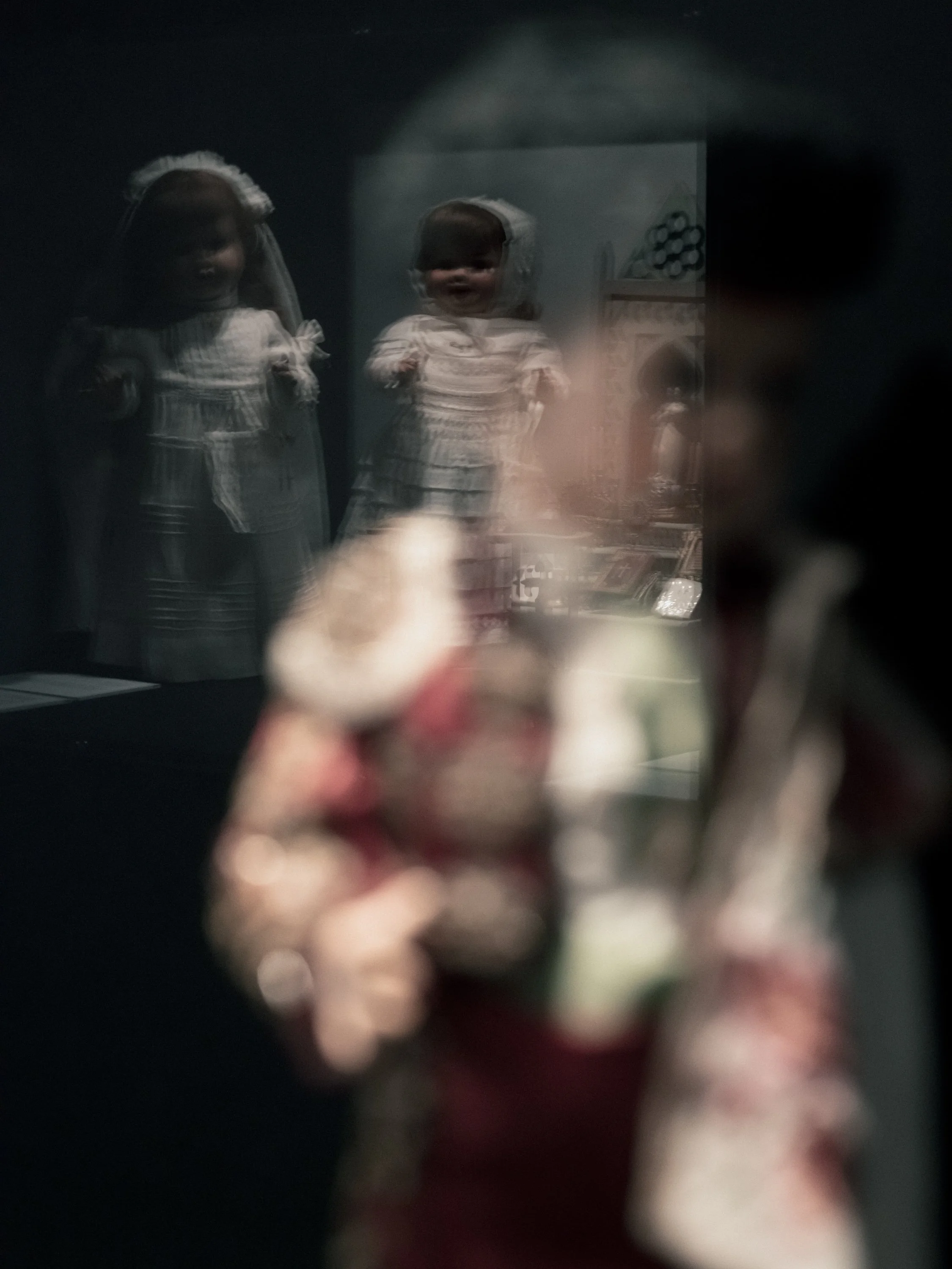 A reflection of two young children wearing dresses with veils, seen through a mirror, with a blurred object in the foreground.