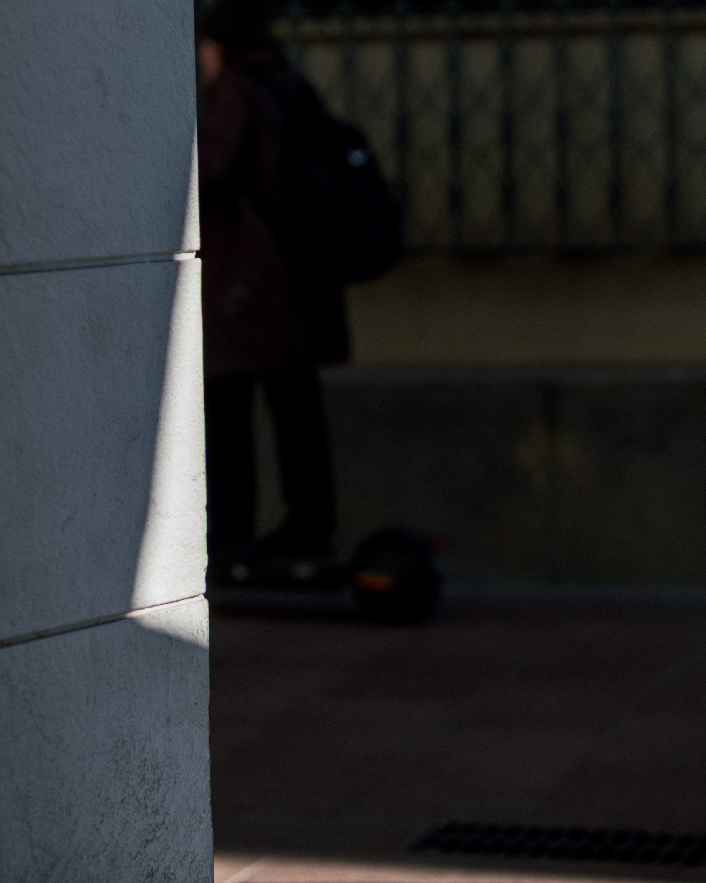 A person is standing next to a wall with a scooter on the ground nearby, partially obscured and in shadow.