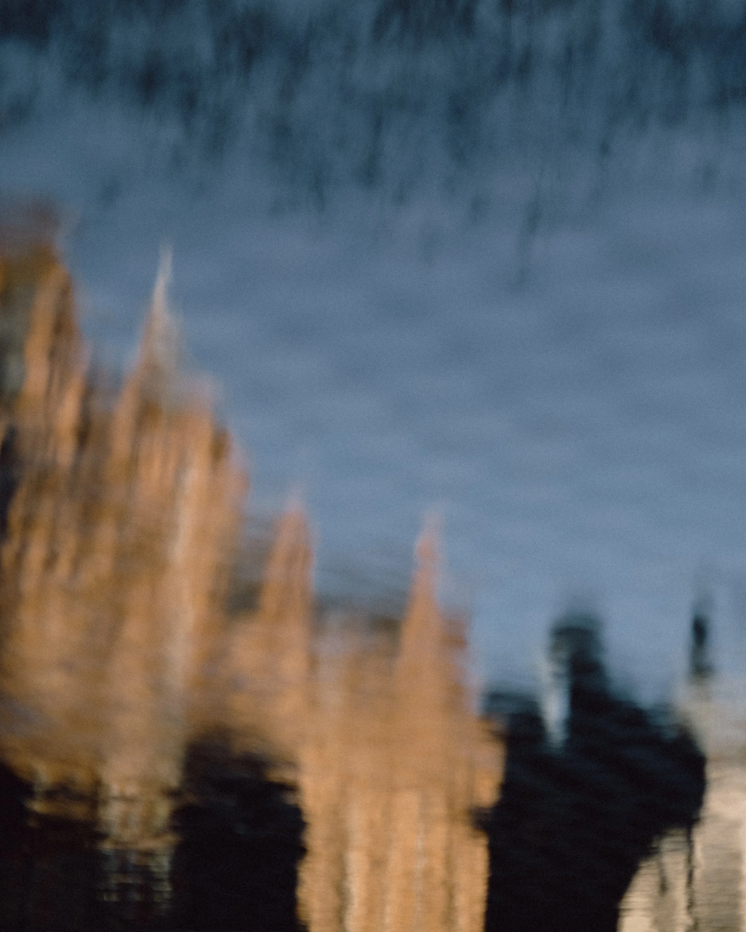 Reflection of a wooden pier and a person standing on a dock in water.