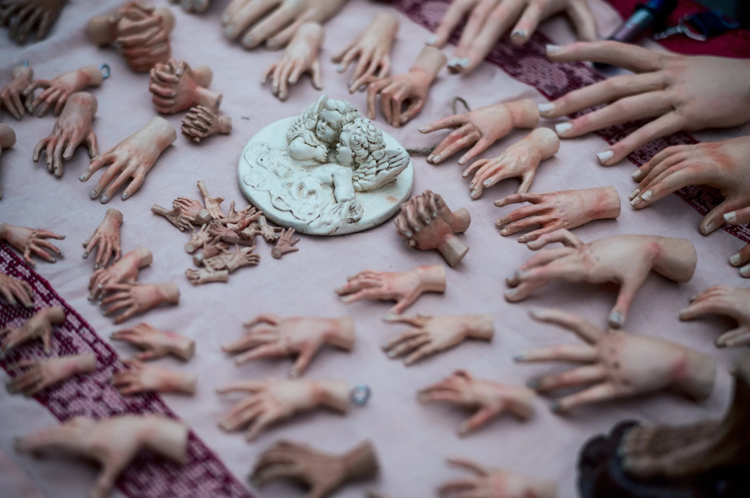 Collection of ceramic figurines of hands, arms, and cherubs arranged on a fabric surface with a central decorative plaque depicting two children kissing.