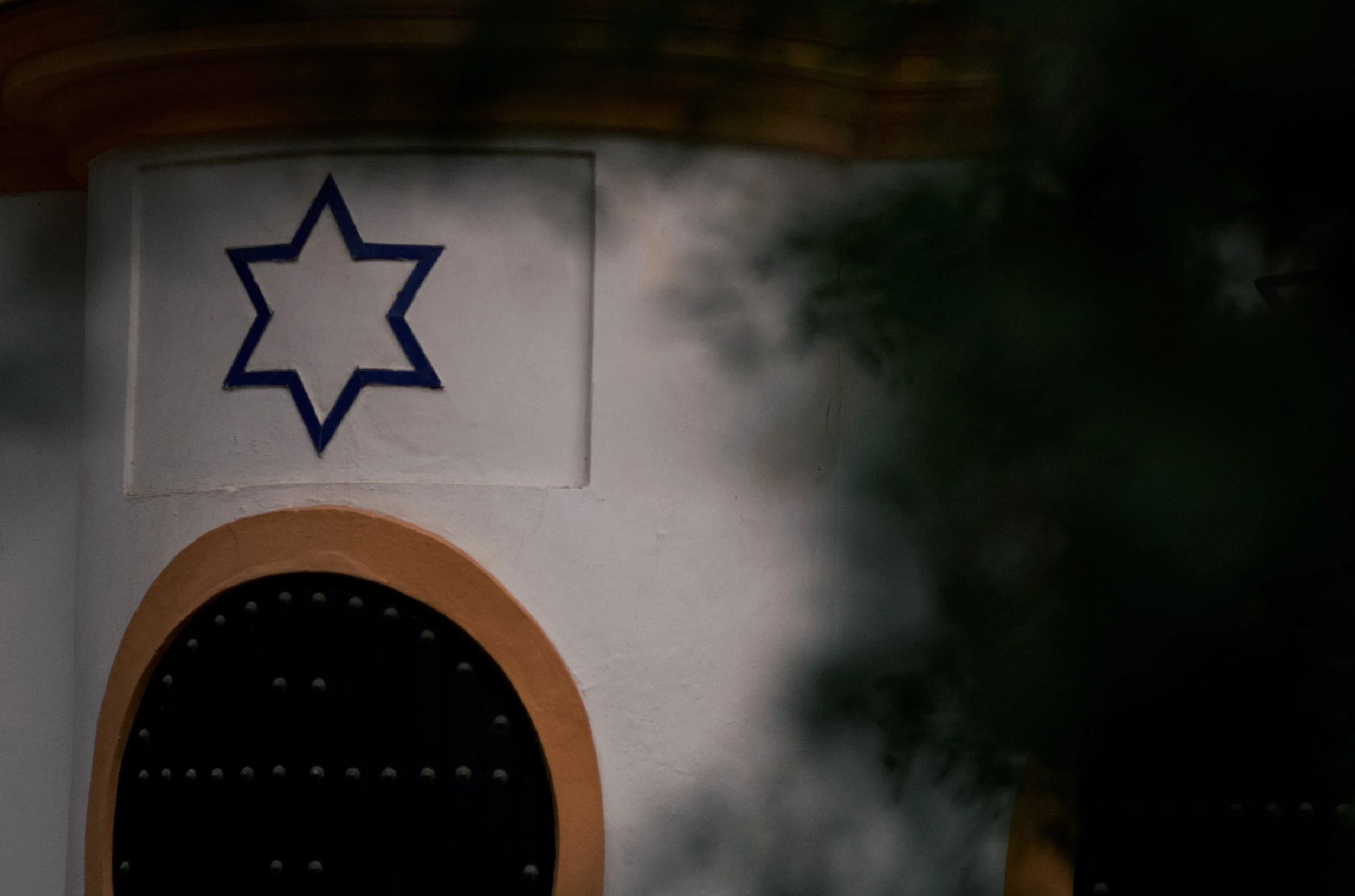 Close-up of a decorative wall feature with a black, studded archway and a white stucco wall with a blue six-pointed star outline in a square panel above.