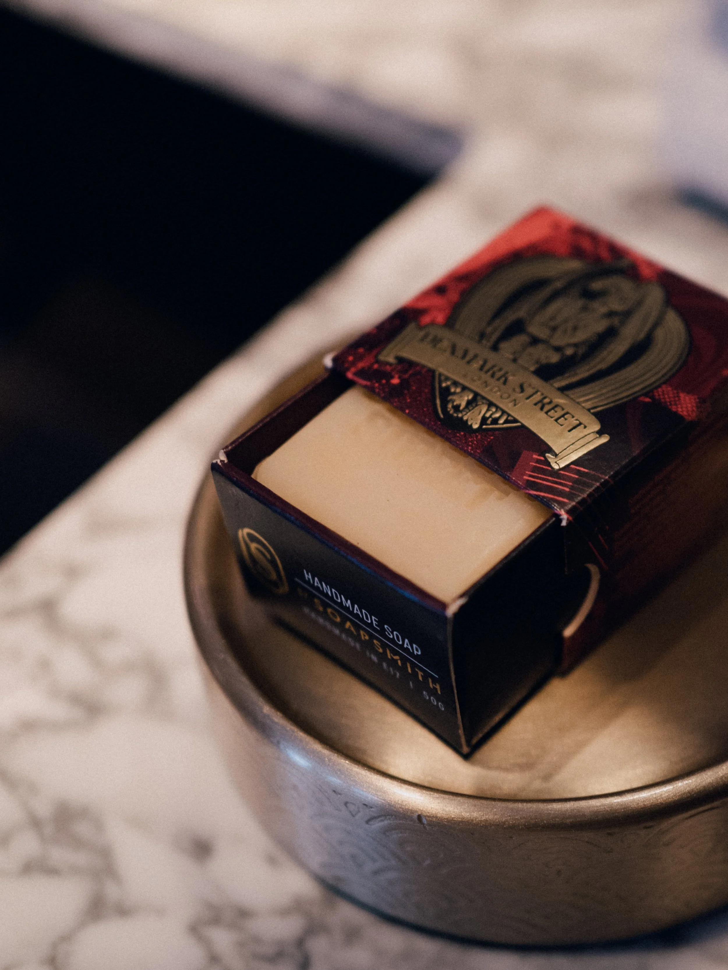 Close-up of a bar of handmade soap with red and black packaging, placed on a metallic soap dish.