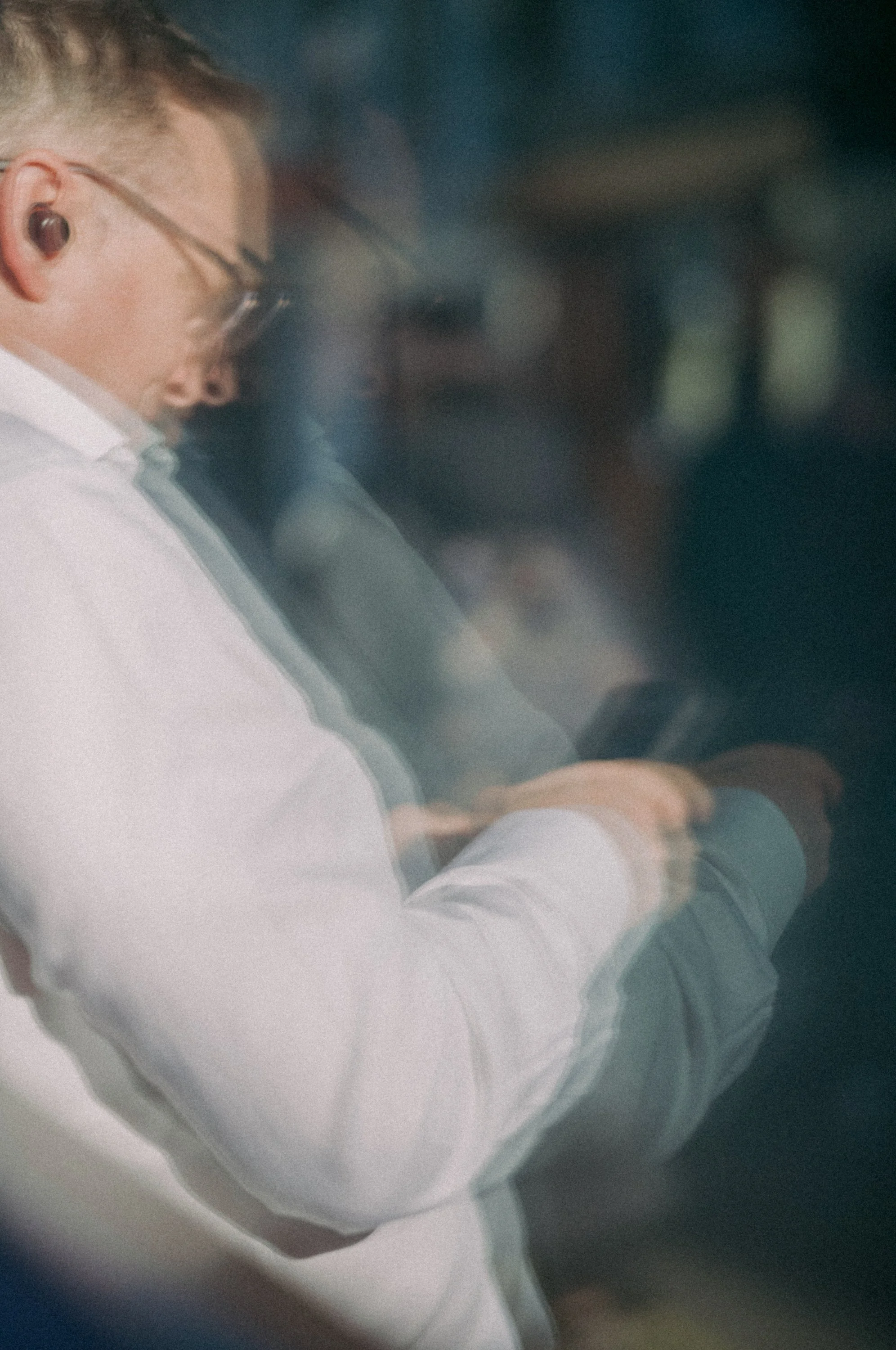 A person wearing a white shirt and glasses, and listening to wireless earbuds, looking at a smartphone.