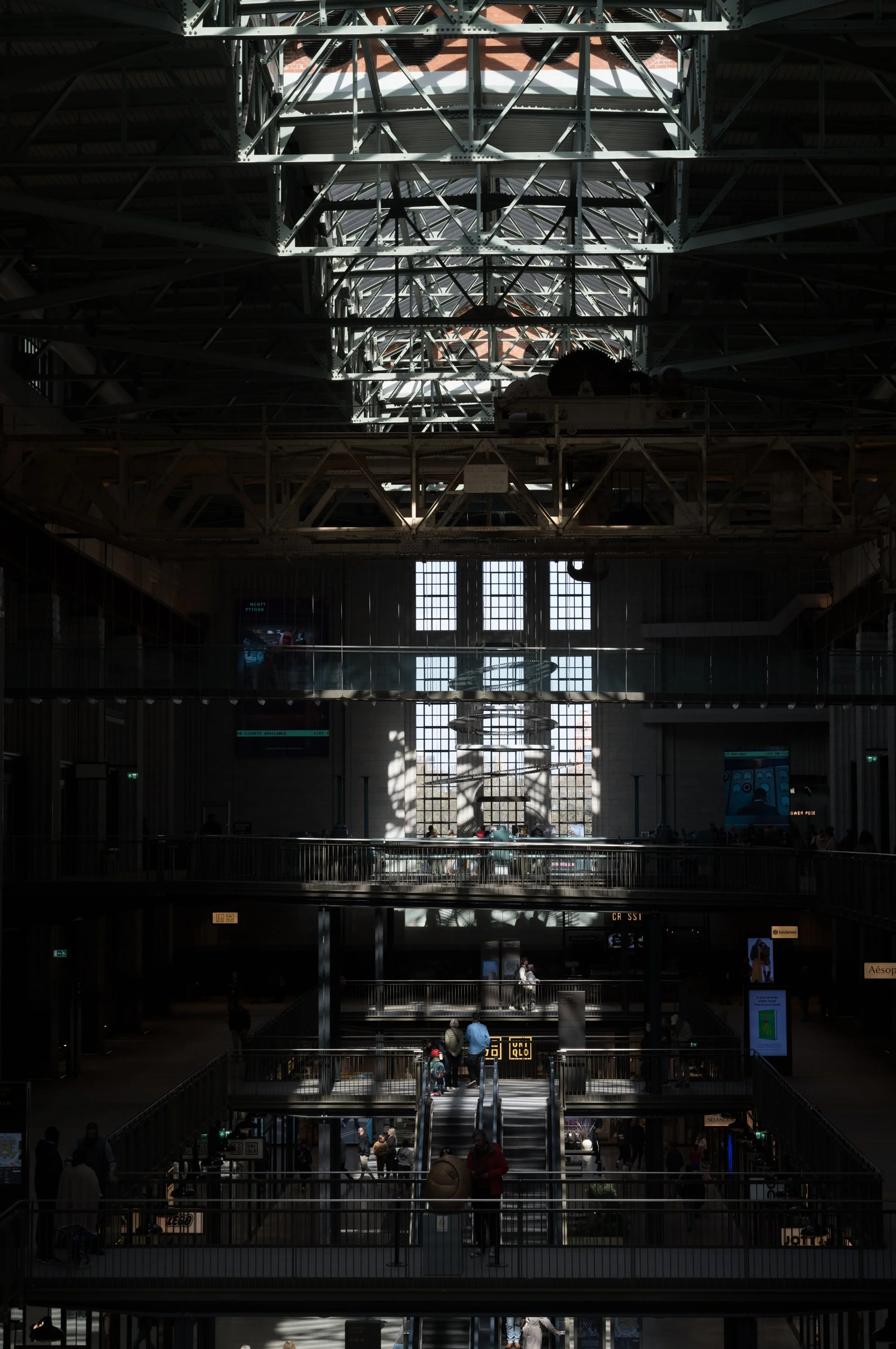 Interior of a large train station with high glass ceiling and multiple levels, featuring escalators and people walking around.