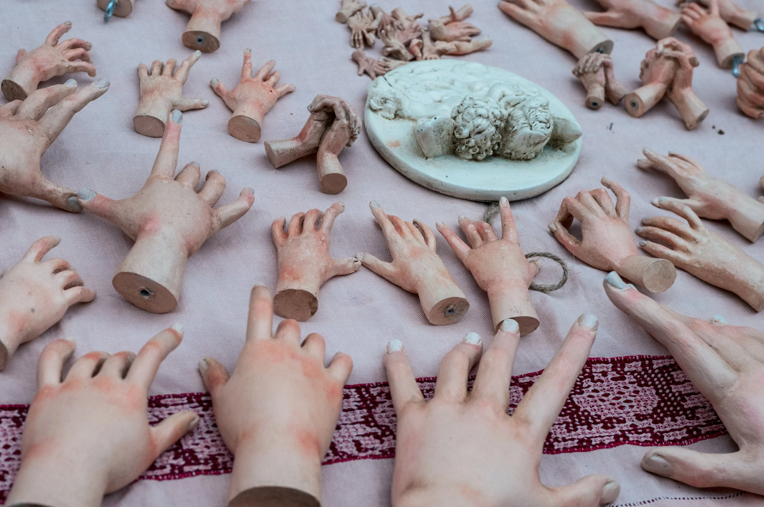 Collection of ceramic or plaster hands and limbs, some attached to small round bases, laid out on a pinkish cloth, with a small sculpture of a face or head among them.