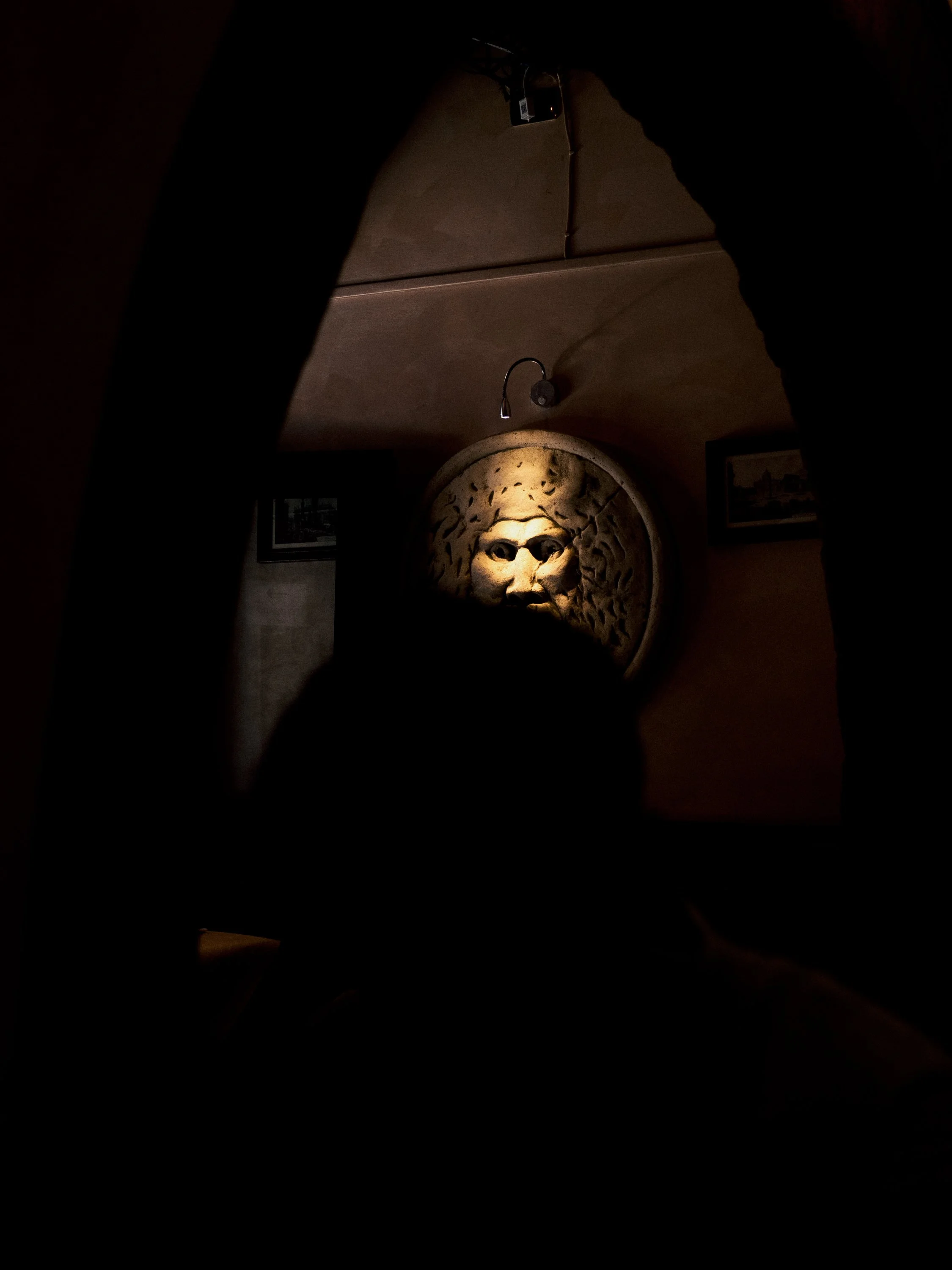 A dimly lit room with a carved stone lion's face sculpture and framed pictures on the wall.