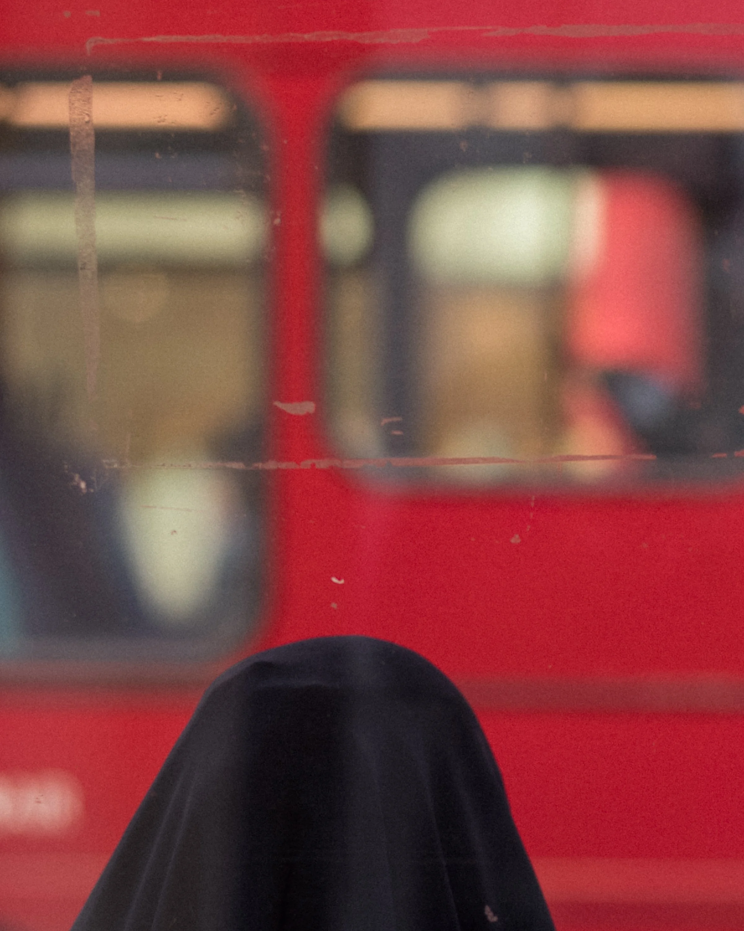 Close-up of a person's knee covered in black fabric, with blurred red, black, and beige objects in the background.
