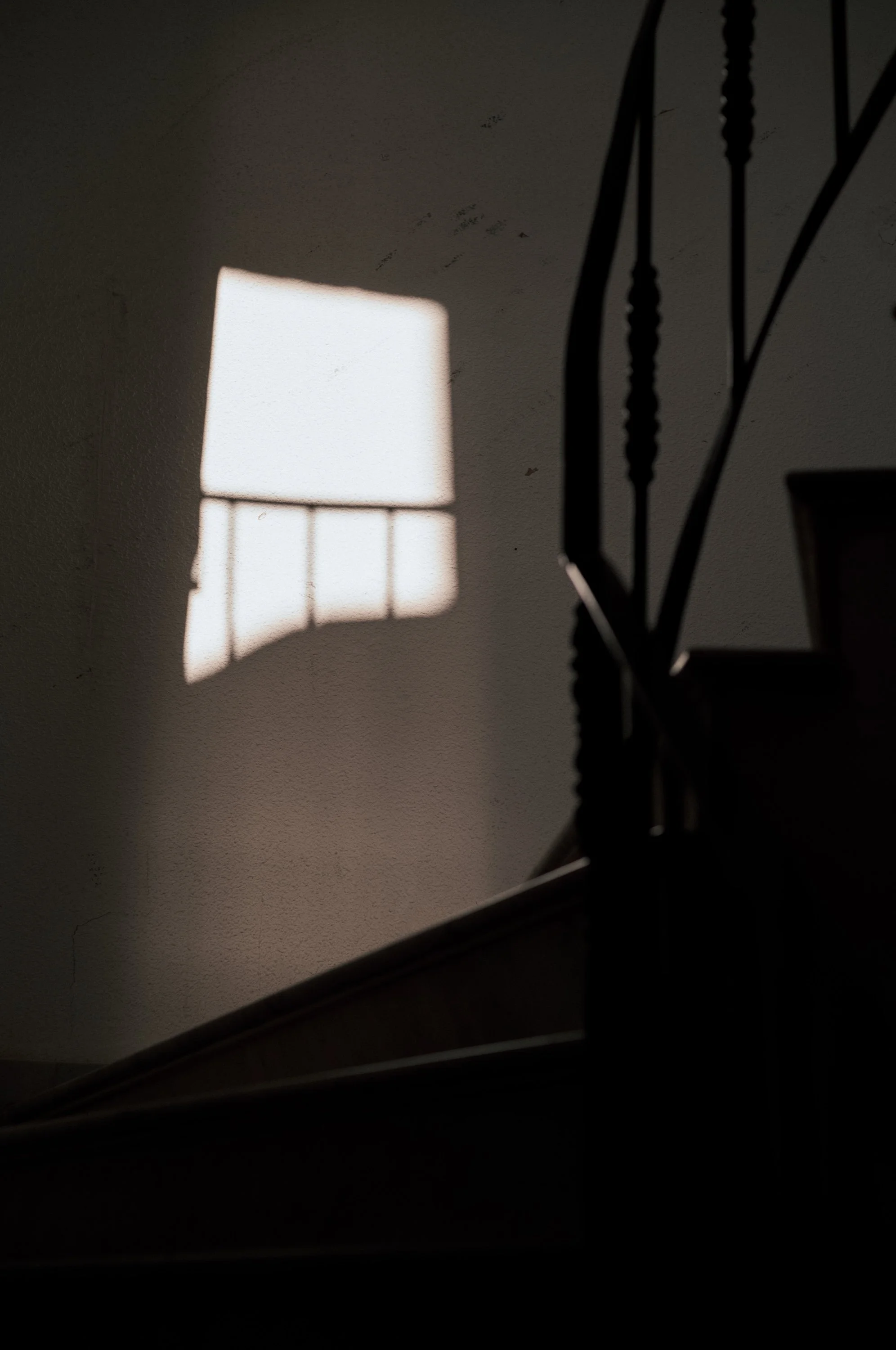 Sunlight casting a shadow of a window with four panes on a wall near staircase railing.