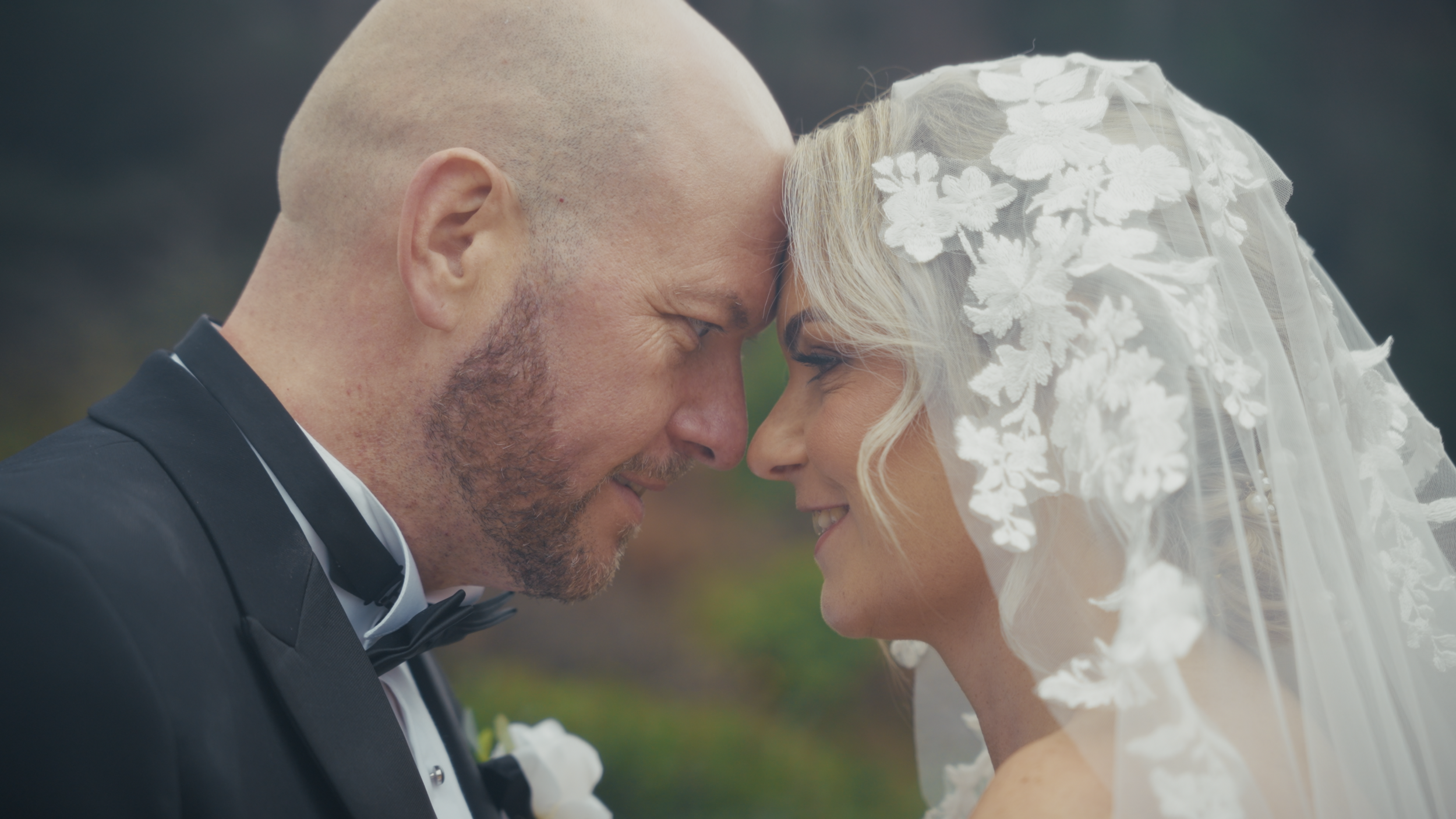 A bride and groom with foreheads touching, smiling, close-up of their faces on wedding day.