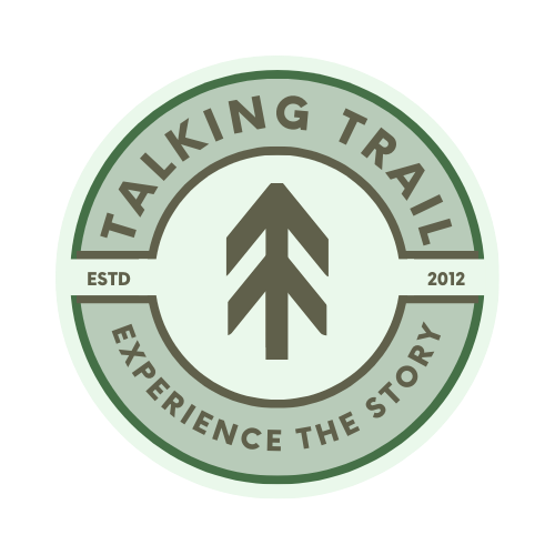 Circular logo with green and beige colors, featuring the words "Talking Trail" at the top, "Experience the Story" at the bottom, and "ESTD 2012" on either side of a central arrow design.
