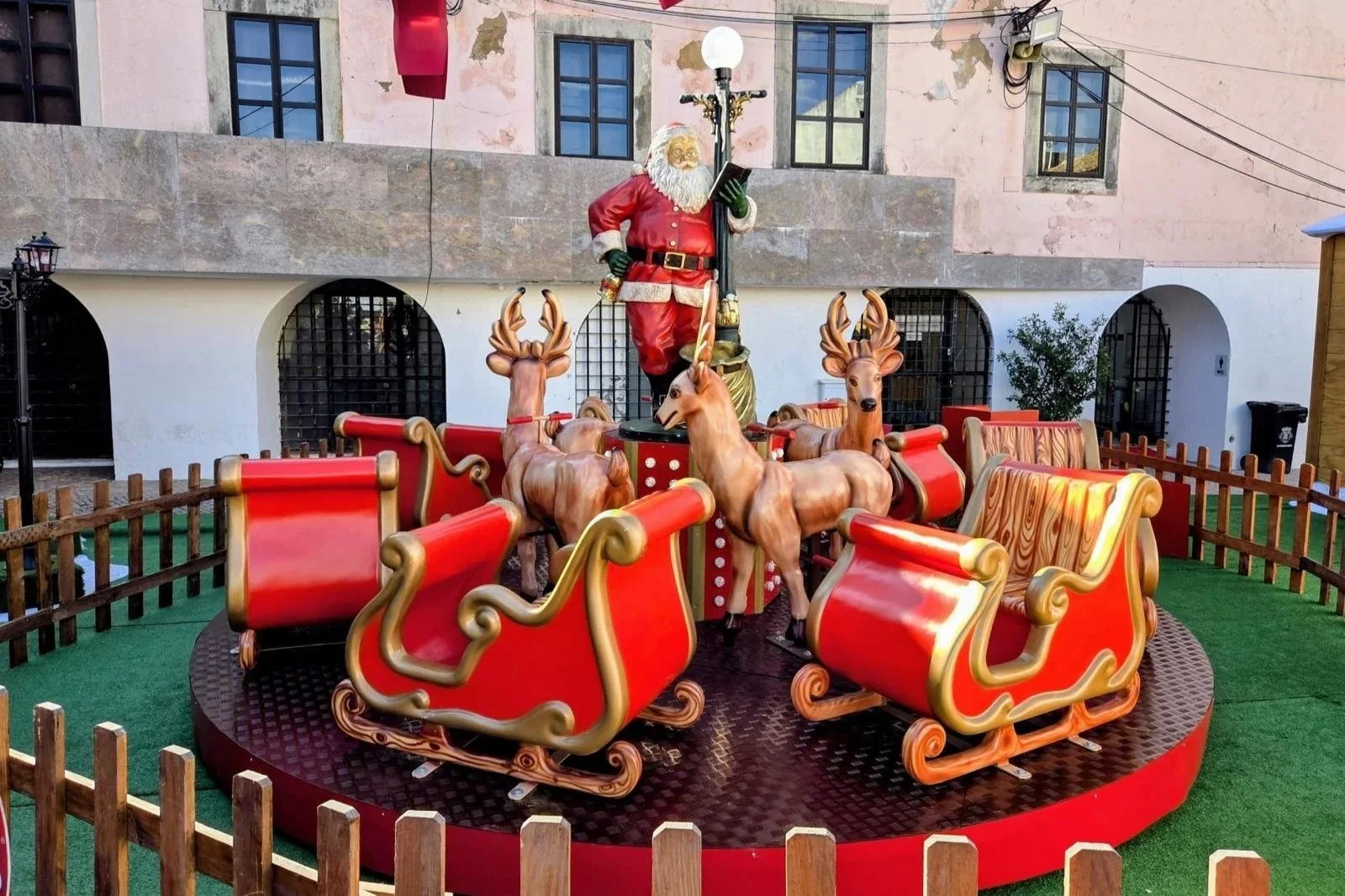 Decoração de Natal com trenó, renas e Papai Noel em uma praça ao ar livre.