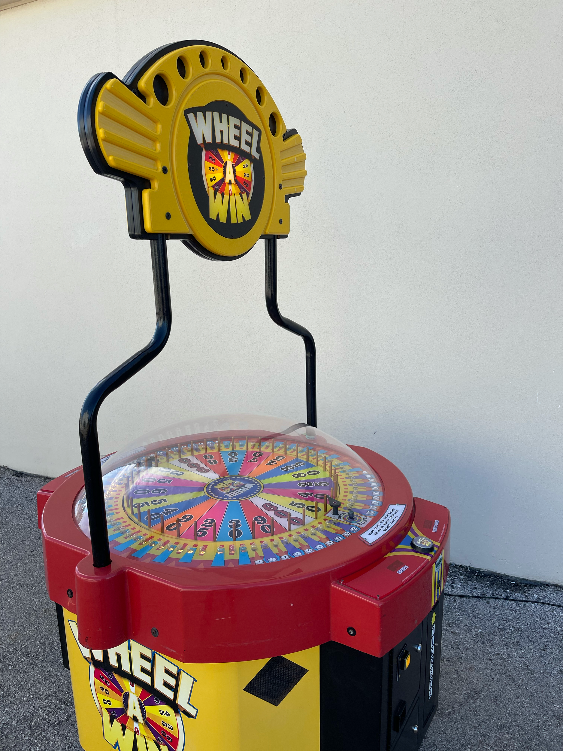Máquina de roda da fortuna colorida com detalhes em vermelho, amarelo, preto e azul, com o nome 'Wheel of' visível na placa frontal.