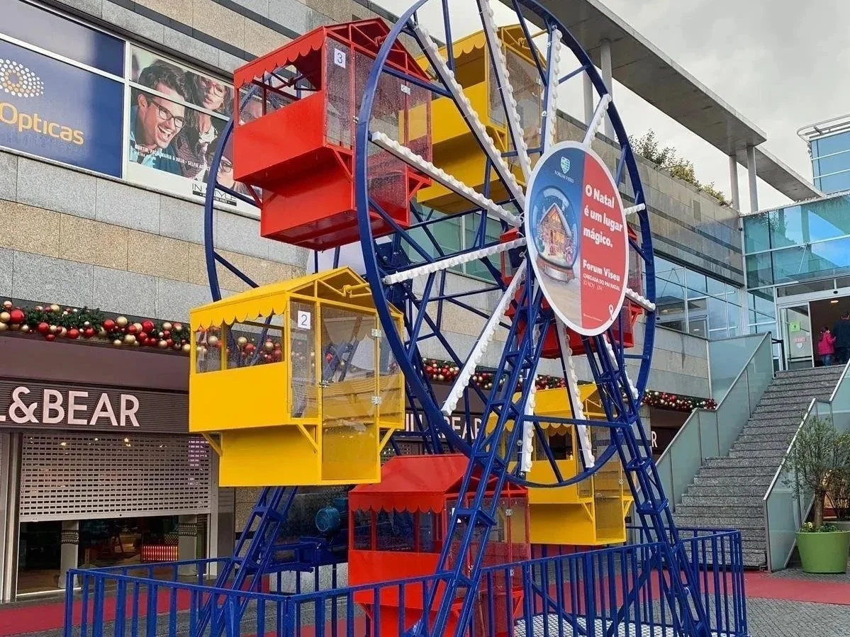 VLT Feriado de Natal com uma roda gigante colorida em um shopping, decorada com enfeites natalinos.
