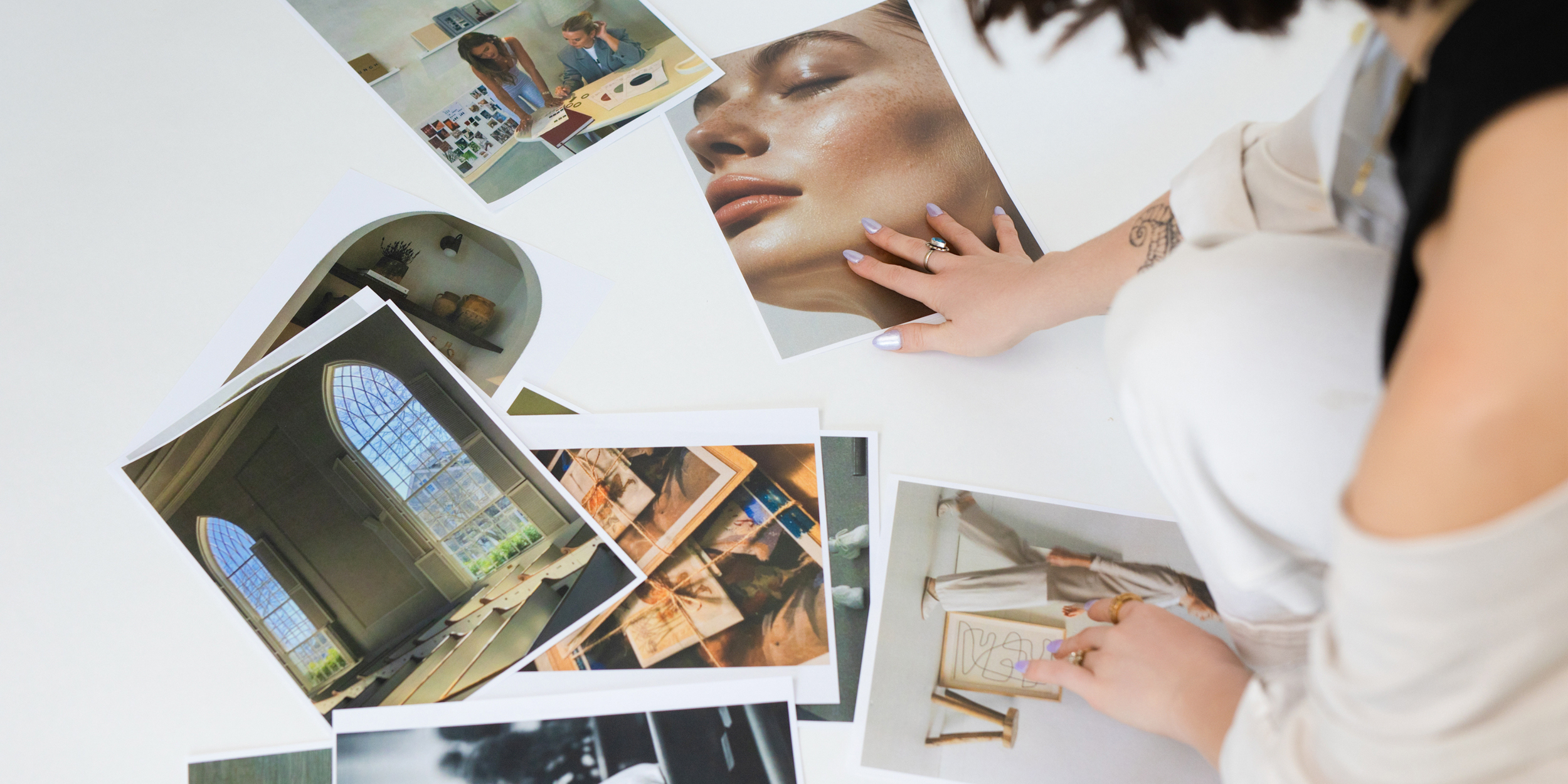 A branding photographer arranging printouts of portrait headshots, interior design, and lifestyle photography onto a white floor to create a visual moodboard for a creative client session.
