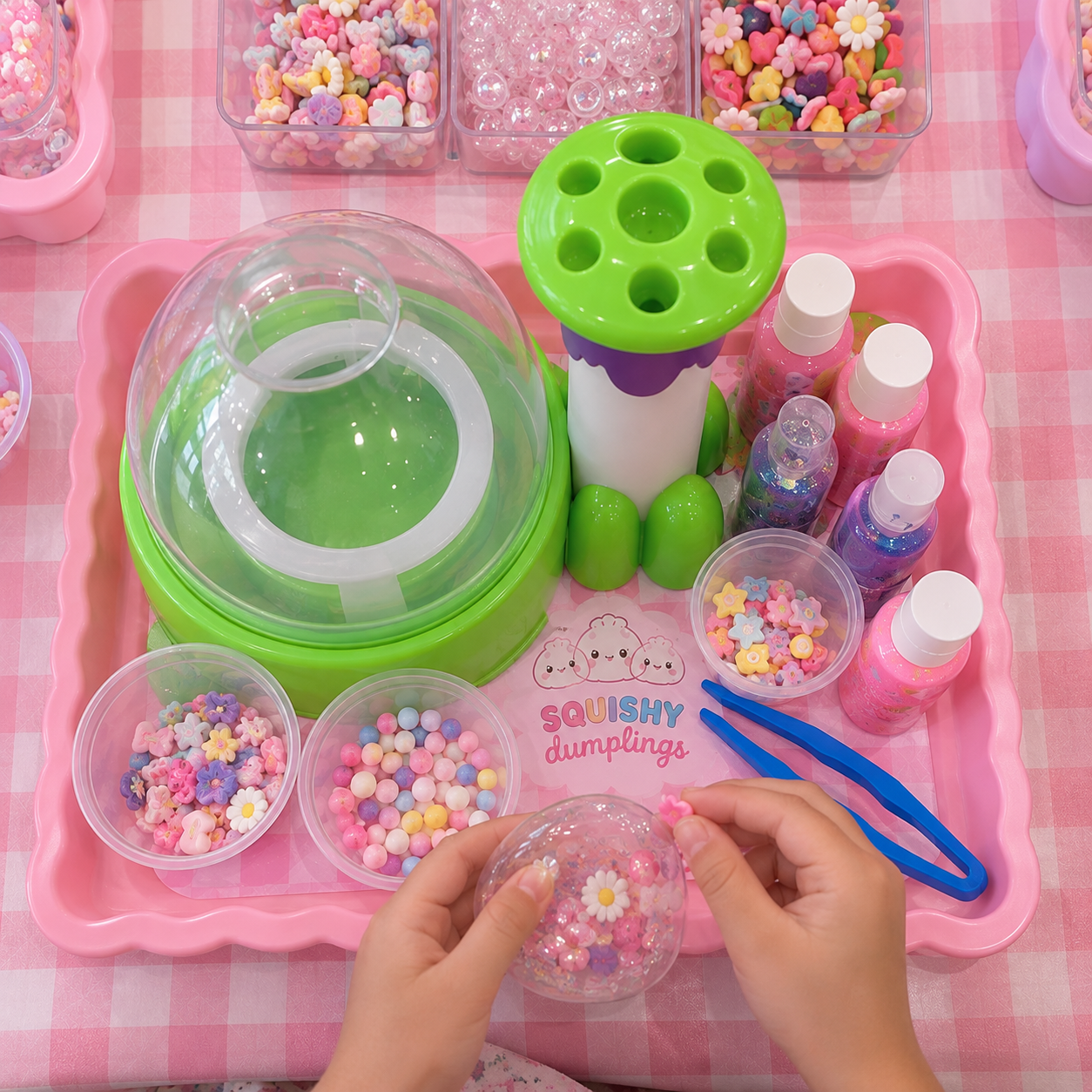 A children's craft or slime-making kit with various colorful beads, glitter, and tools on a pink checkered table.