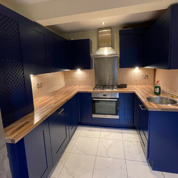 Modern U-shaped kitchen with blue cabinets, wooden countertops, beige tile backsplash, stainless steel oven and range hood, small sink, and a bottle of dish soap.