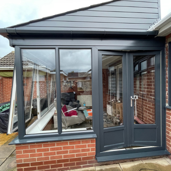 Enclosed porch with large glass windows and a door, attached to a brick house.