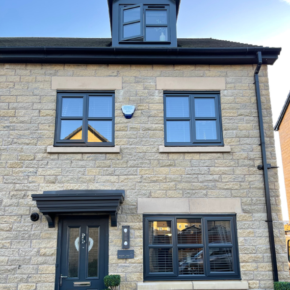 Front view of a new brick house with black-framed windows, a black front door, and a small window in the roof. The house has a modern and clean appearance.