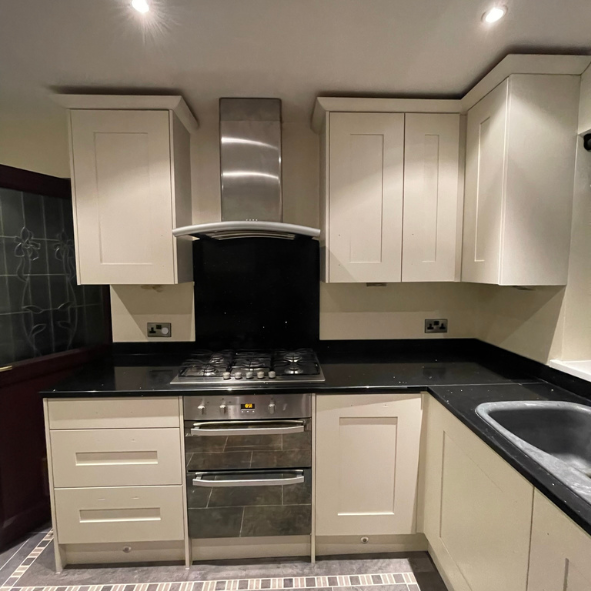 Kitchen with white cabinets, black countertop, stainless steel oven and stove, range hood, and a sink.